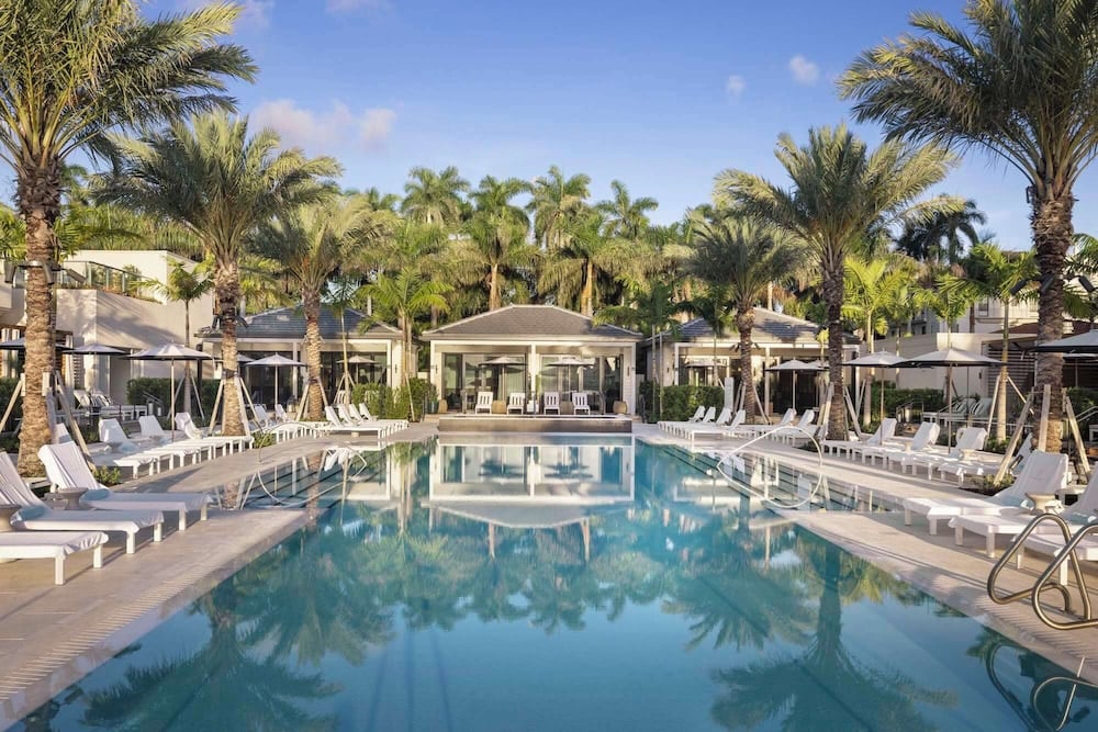 Palm fronds cast gentle shadows over crystalline waters where white loungers invite endless afternoons beneath Florida's impossibly blue sky at this sophisticated adults-only retreat.