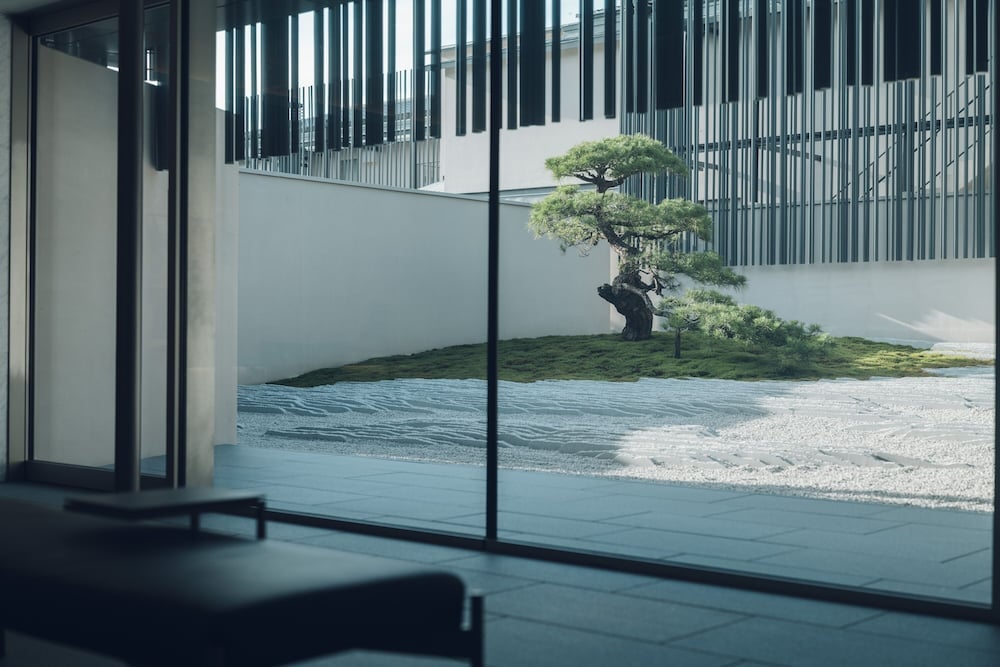 Floor-to-ceiling windows frame a contemplative Japanese garden where a sculptural pine tree anchors raked gravel patterns, blurring the boundaries between inside and out.