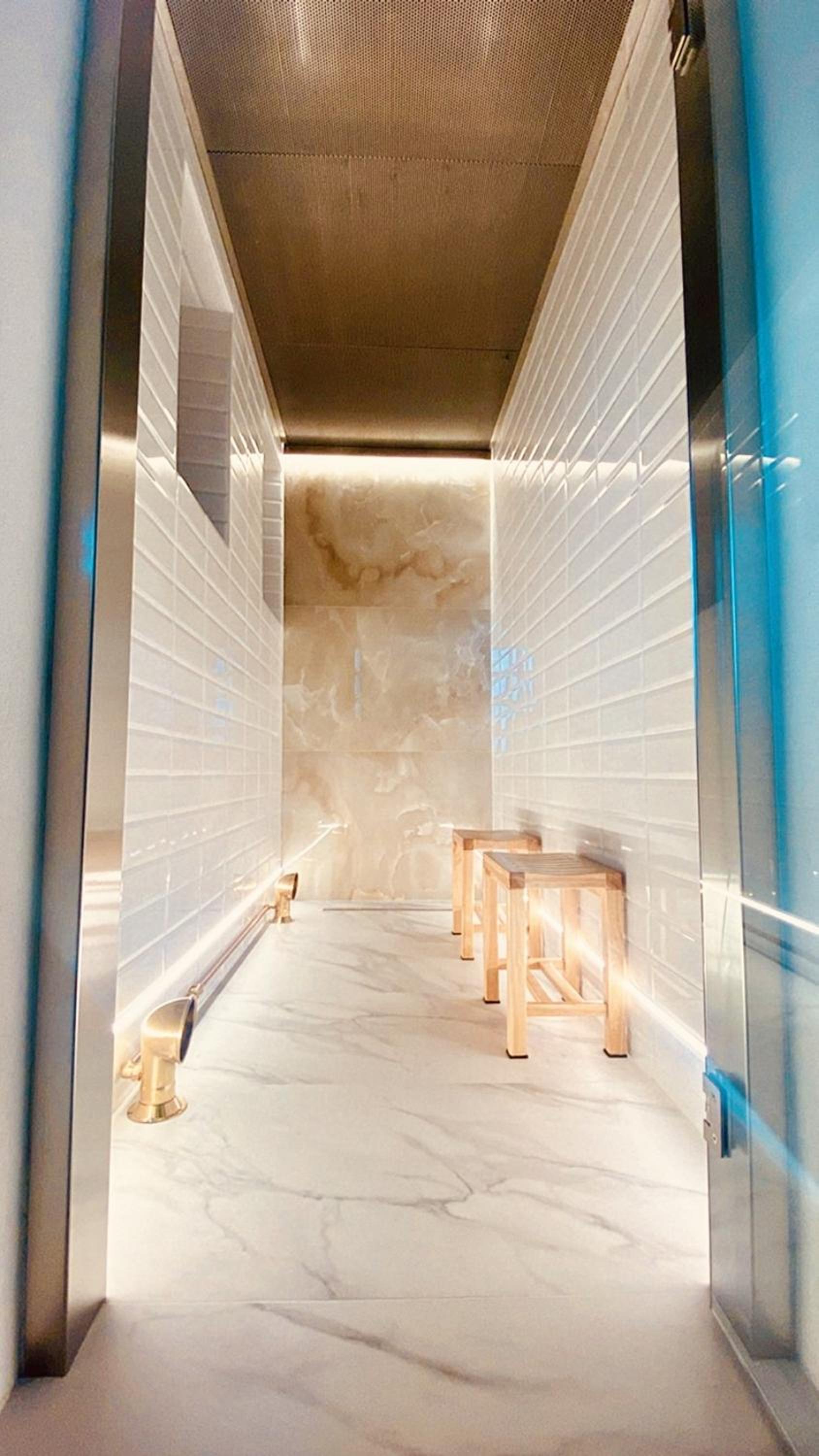 Sculptural marble walls curve dramatically around heated benches in this temple-like sauna, where warm light filters through ribbed stone creating an otherworldly cocoon.