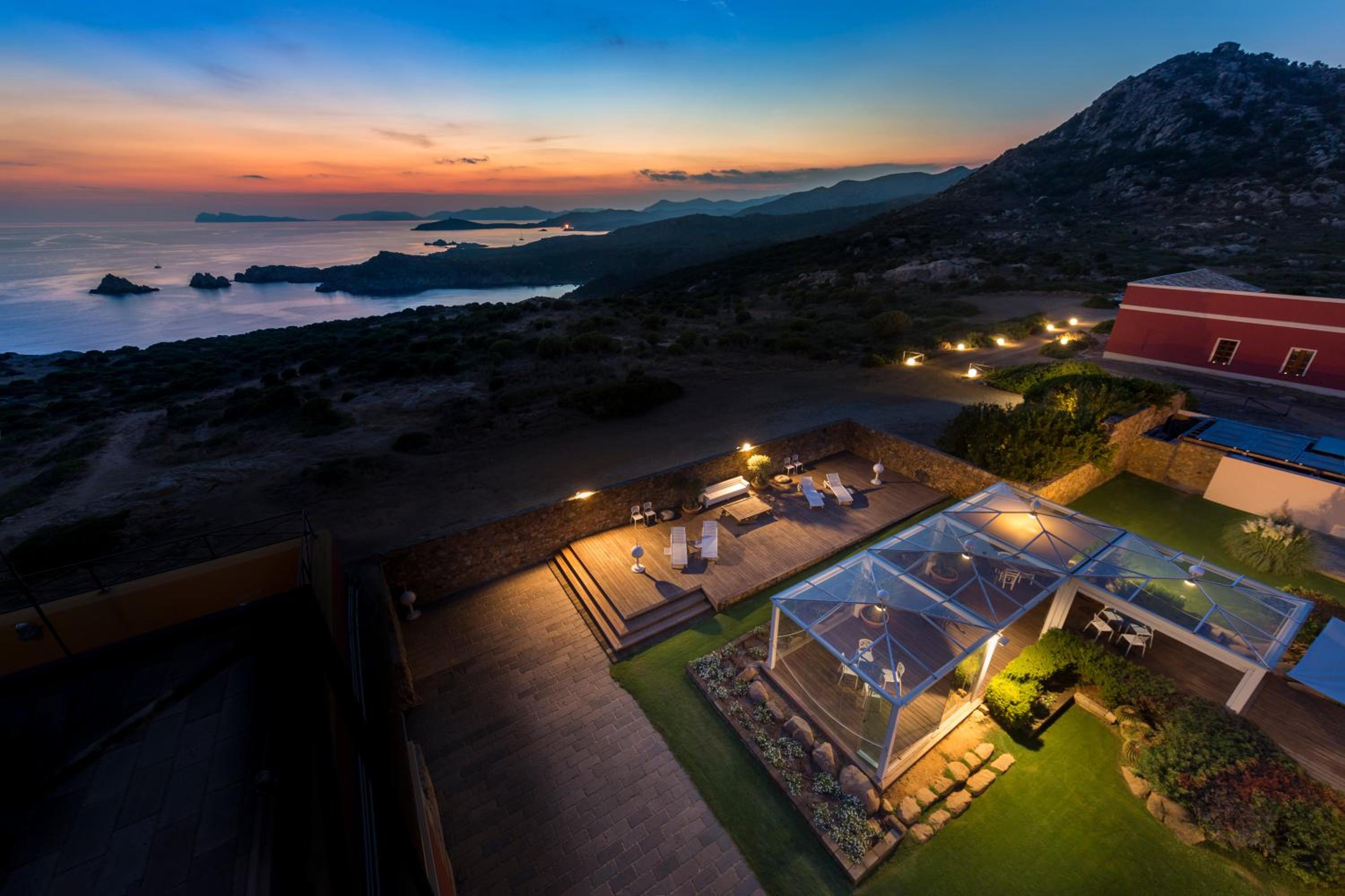 Twilight transforms this hillside retreat into a glowing sanctuary, where glass pavilions and terraced decks frame the dramatic coastline stretching toward distant islands.