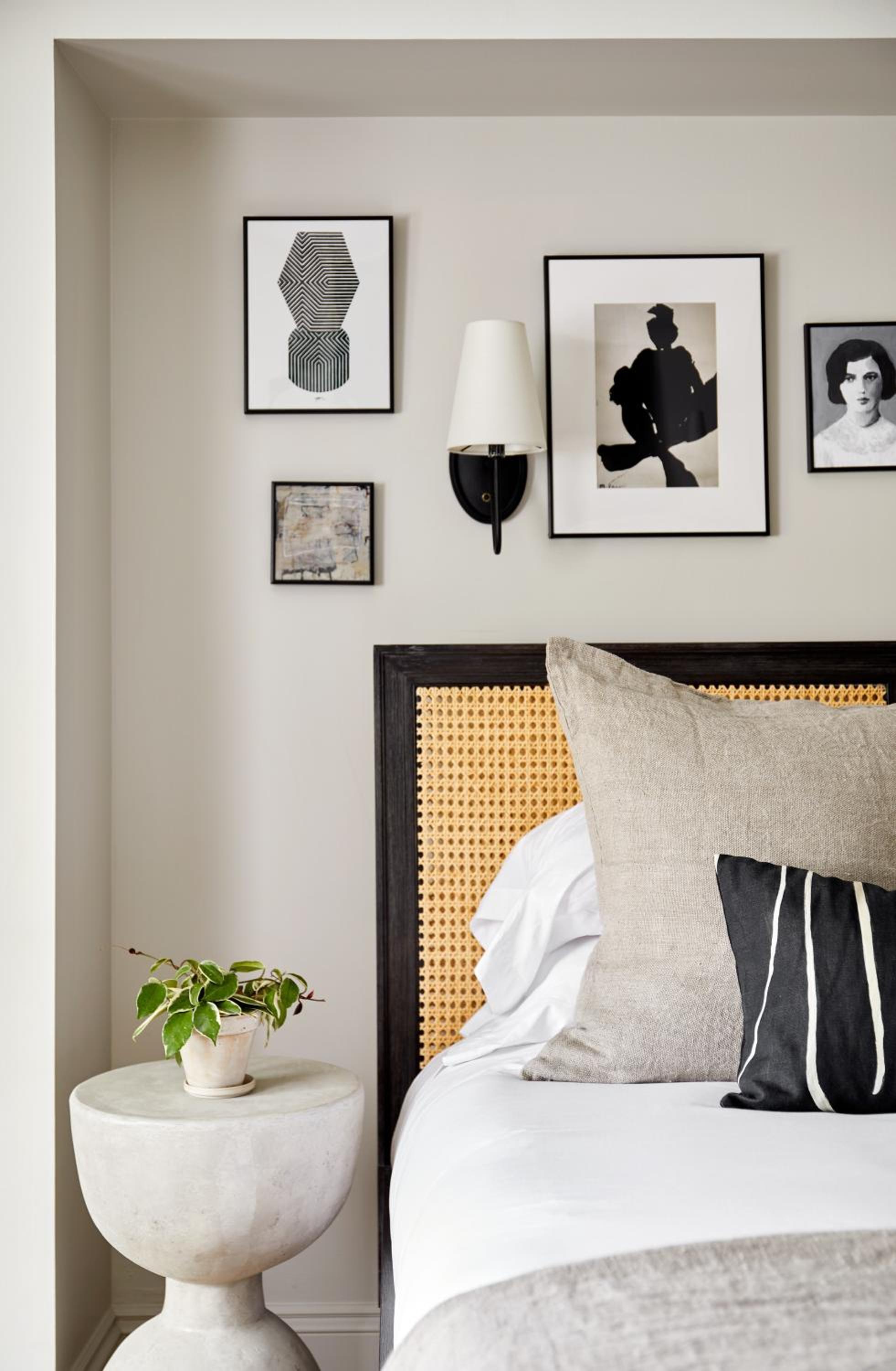 Curated artwork and a striking cane headboard create an intimate gallery-like atmosphere, where crisp linens meet thoughtful design touches and warm sconce lighting.