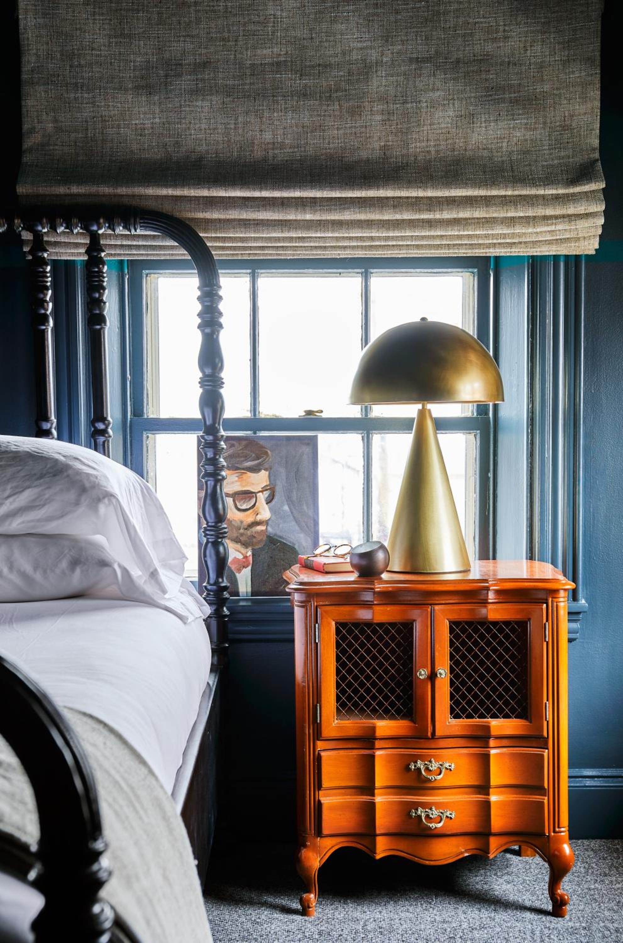 Rich navy walls frame a brass mushroom lamp and cherry nightstand, where natural linen blinds filter Portland's gentle light into this intimate guest room.