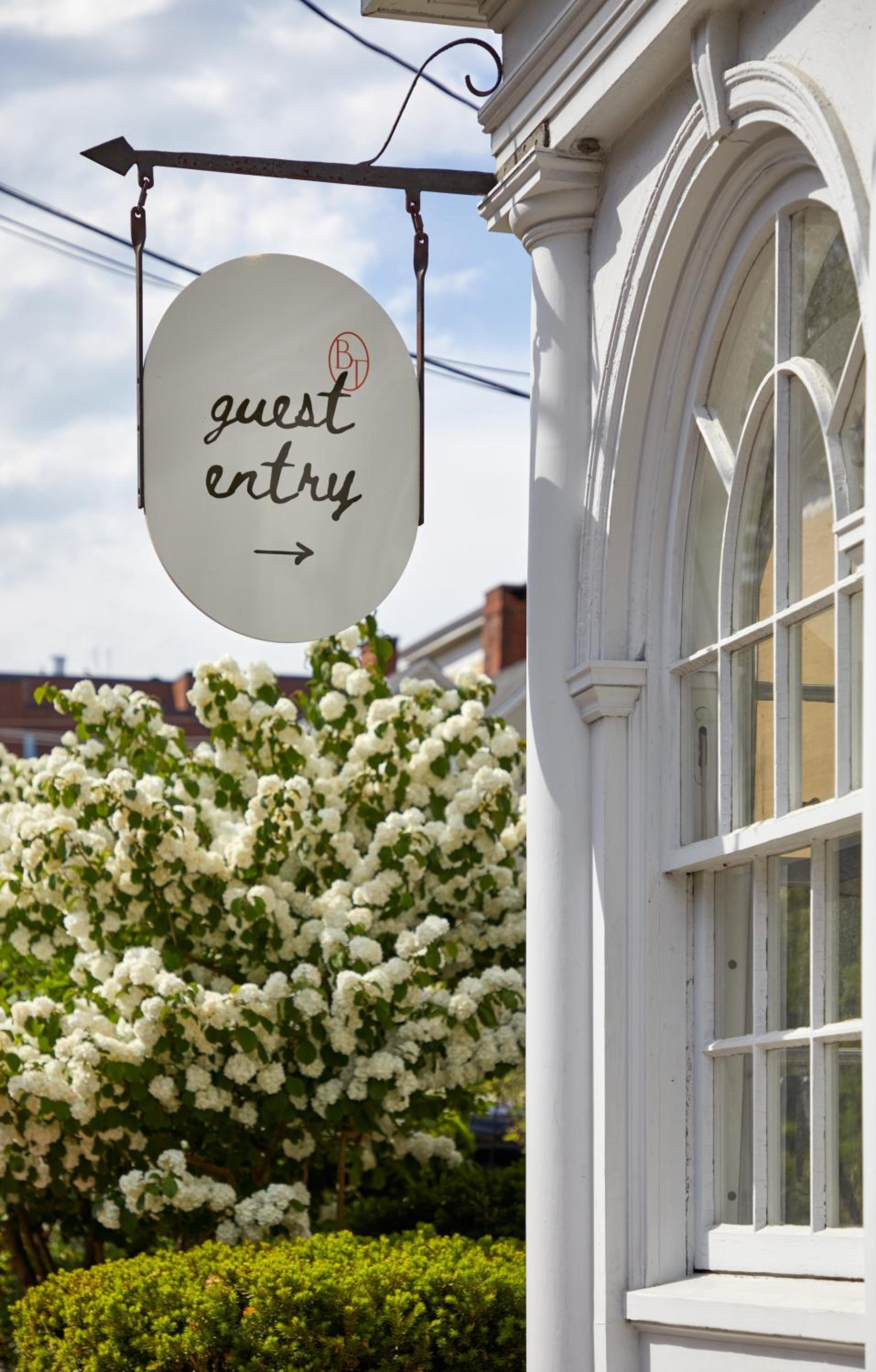 An elegant oval sign marks the guest entry beneath graceful arches, while blooming white hydrangeas frame this charming Portland doorway with classic New England appeal.