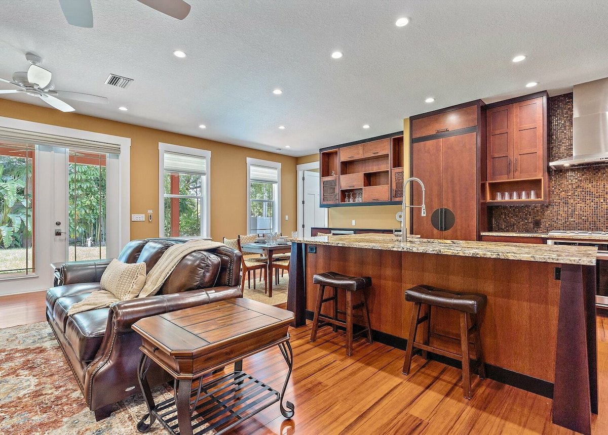 Barstools line the kitchen island and natural light floods the living room and kitchen space.