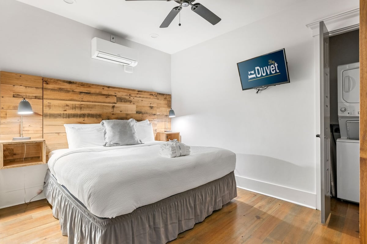 **CAPTION:** Experience modern comfort at "Property" in Charleston, US, where contemporary minimalism meets rustic charm. The room features a cozy king-sized bed against a rustic wooden headboard, creating a warm and inviting atmosphere. Soft white linens and neutral tones enhance the peaceful ambiance, while sleek fixtures and natural materials add to the stylish appeal. Ideal for discerning travelers seeking an elegant yet understated retreat in a vibrant city setting.