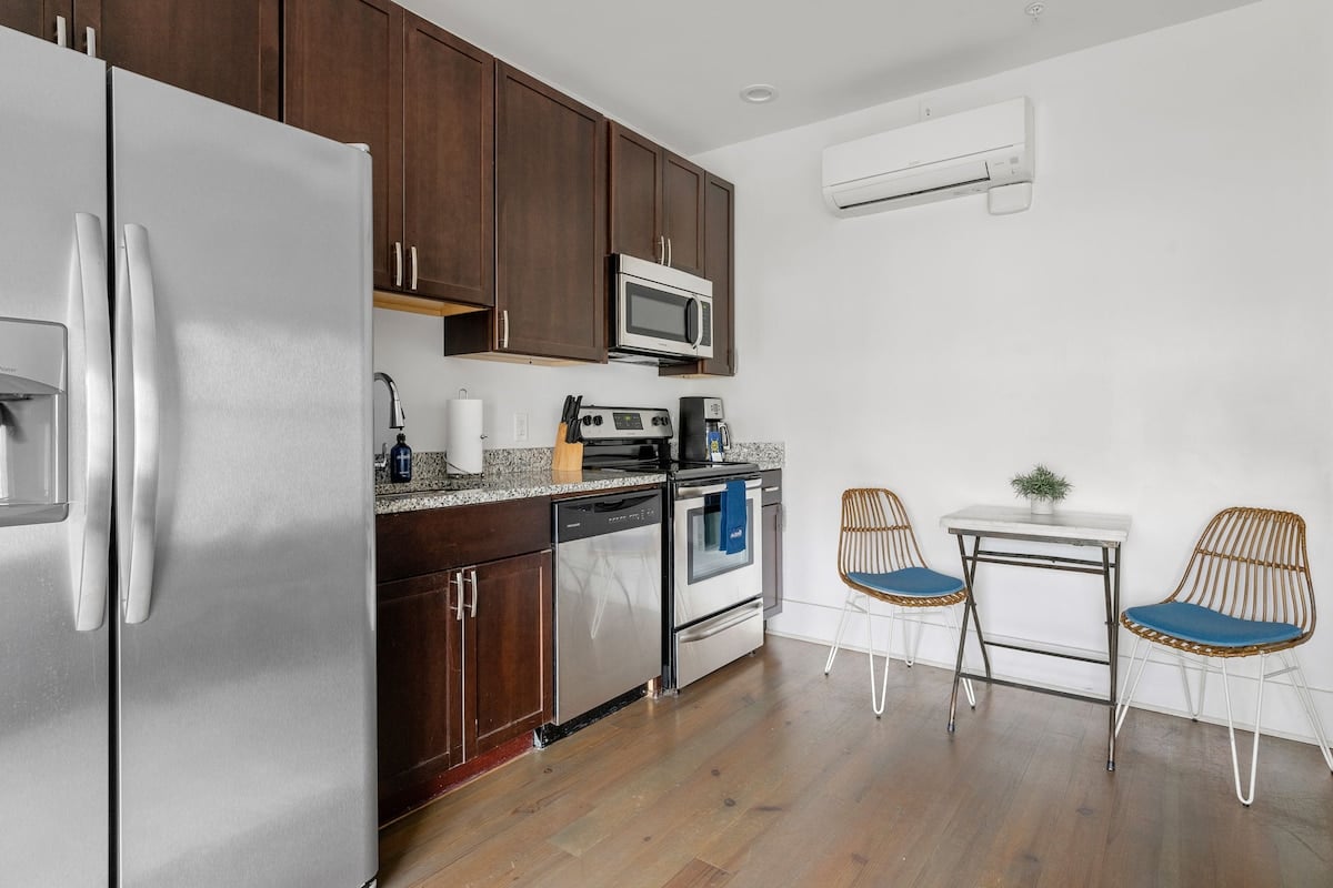 **CAPTION:** 
This modern kitchen at Property in Charleston, US, showcases a sleek, minimalist design ideal for contemporary travelers. The space features dark wood cabinetry, stainless steel appliances, and a granite countertop, exuding a clean and sophisticated ambiance. The open atmosphere is balanced with light wood flooring and white walls, enhancing the room's warm and inviting mood—perfect for a luxurious stay.