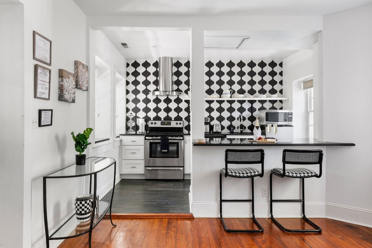 CAPTION:
Experience the modern charm of "Property" in Charleston, US. This luxury travel destination boasts a contemporary interior with a monochromatic black-and-white tile backsplash that creates a striking contrast against clean white walls. The open kitchen concept is complemented by sleek stainless-steel appliances and warm, polished hardwood floors, offering a stylish and inviting atmosphere for discerning travelers seeking comfort and elegance in every detail.