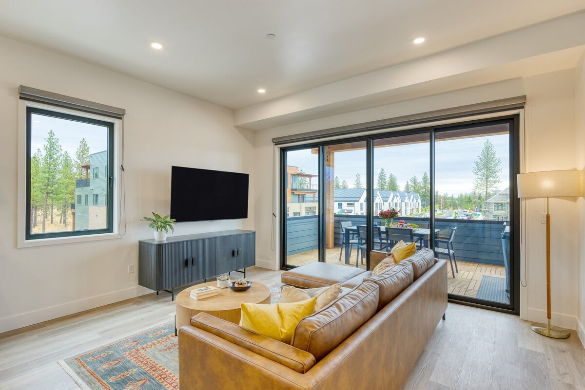 **CAPTION**: Nestled in Bend, US, Property showcases a contemporary architectural style with a warm and inviting atmosphere. The interior features a sleek, modern design with clean lines and expansive windows that let in natural light. Dominated by neutral tones and accented with warm browns and vibrant yellows, the space offers a perfect blend of comfort and elegance. The open plan living area, leading to a spacious deck, is ideal for travelers seeking relaxation and scenic views.