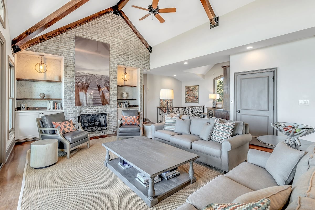 **CAPTION**: Discover luxury at "Property" on Seabrook Island, showcasing a charming blend of rustic and contemporary architectural style. This inviting space features exposed wood beams and a brick fireplace, setting a cozy, elegant atmosphere. The neutral color palette of soft grays and beiges enhances its modern appeal, providing a warm, welcoming retreat. Perfect for travelers seeking serene relaxation and sophisticated comfort in a picturesque setting.