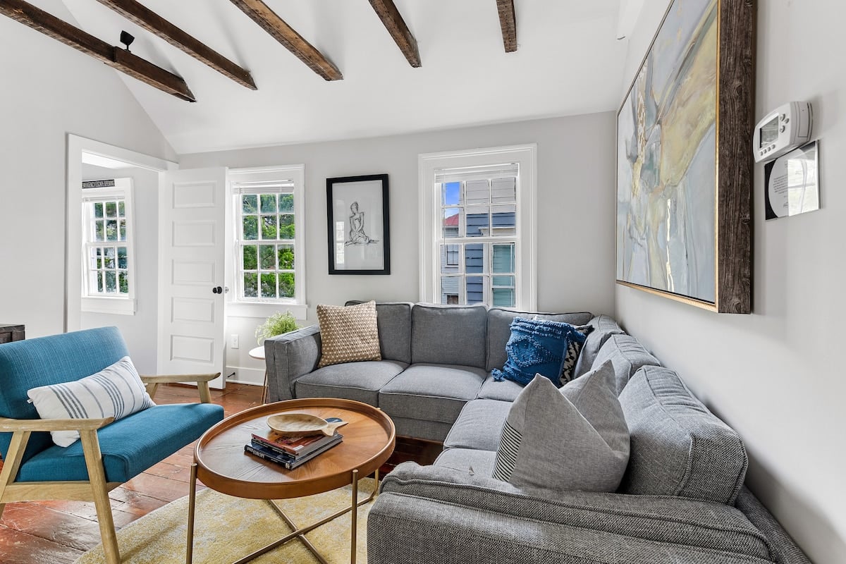 CAPTION:  
"Property in Charleston showcases a charming blend of classic Southern architecture and modern comfort. This inviting space features exposed wooden beams and a neutral color palette, highlighted by soft grays and calming blues. Sunlight pours through large windows, illuminating the cozy seating area adorned with contemporary art. Ideal for travelers seeking relaxation and historical charm, this luxury retreat promises an authentic Charleston experience."