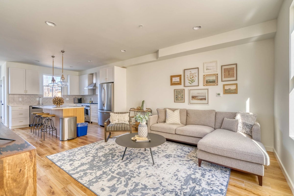 CAPTION:
This luxurious "Property" in Portland showcases a modern architectural style with a cozy yet sophisticated atmosphere. The open-concept living area is designed with a neutral color palette, combining soft grays and warm wood tones. Key visual elements include a contemporary L-shaped sofa, a stylish rug, and kitchen with sleek cabinetry and stainless steel appliances. Ideal for travelers seeking a blend of style and comfort, this space offers a welcoming retreat.