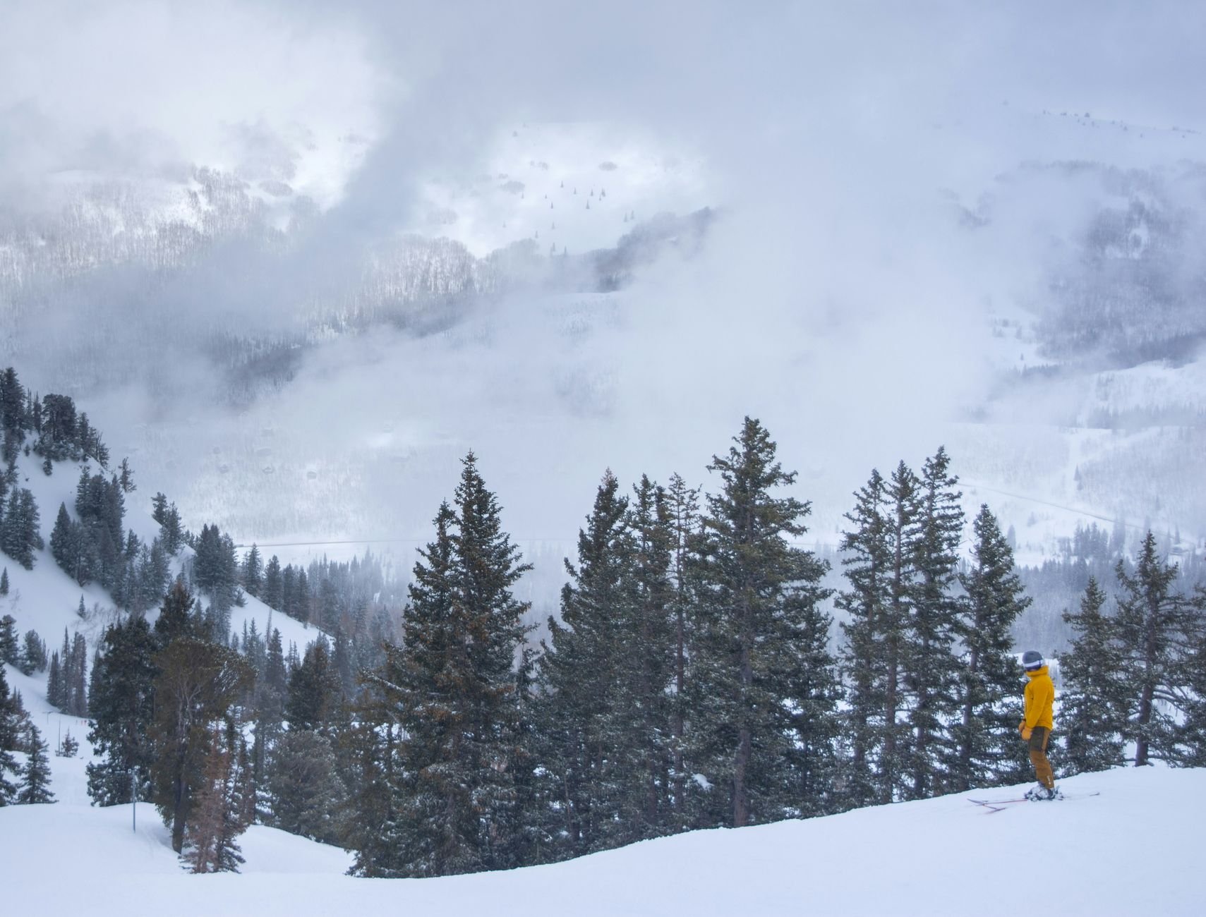 A skier in a yellow jacket enjoys a snowy day at Brighton Resort, Utah's alpine landscape.