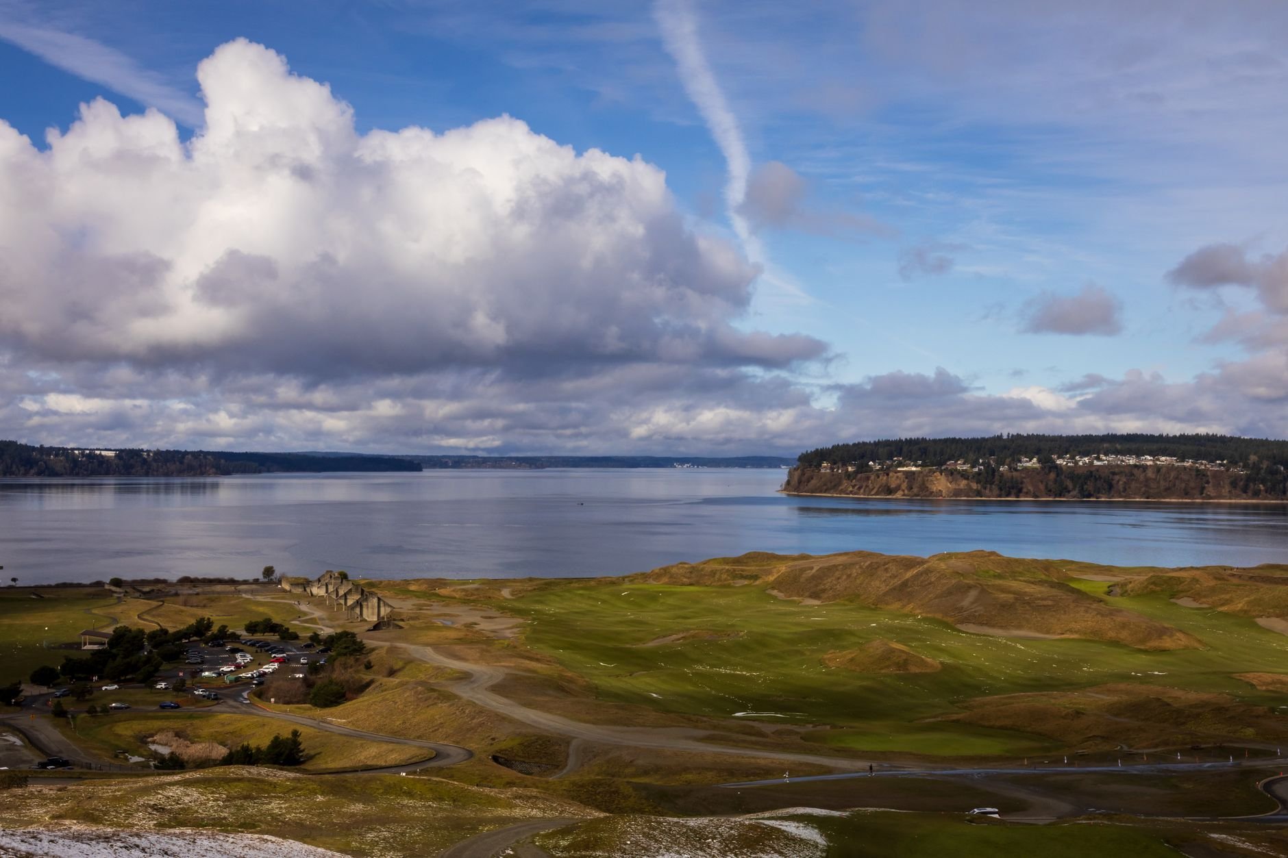 Stunning aerial view of a coastline with a golf course, surrounded by cloudy skies and calm waters.