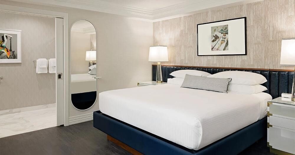 Crisp white linens complement the navy velvet headboard in this serene suite, where warm lamplight creates intimate pools of illumination against textured wallpaper.