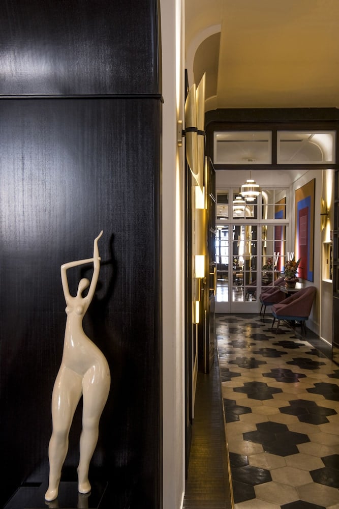 Elegant sculptural figure graces dark wood paneling while geometric tile flooring leads toward the warmly lit lobby, creating an sophisticated interplay of art and architecture.