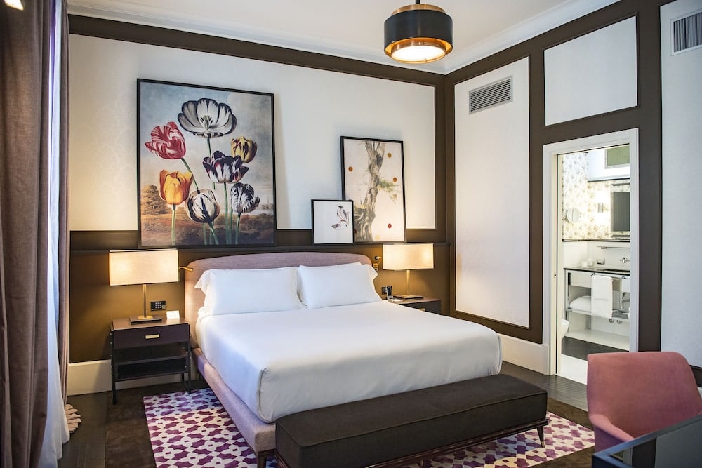 Dark wood frames and botanical prints create intimate drama in this sophisticated guest room, where geometric carpets add playful contrast to crisp white linens.