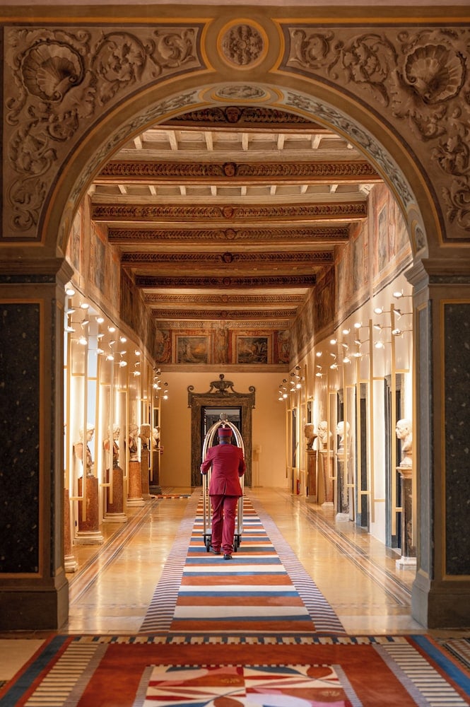Ornate Moorish arches frame a grand corridor where intricate ceiling frescoes and geometric floor tiles create a mesmerizing perspective toward the ornamental doorway beyond.