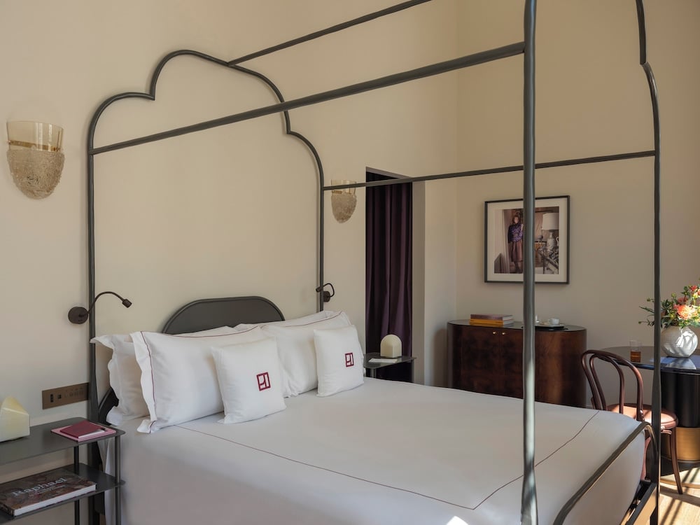 Crisp white linens and minimalist metal four-poster frames create serene sanctuaries, where natural light filters through heavy curtains onto polished stone floors.