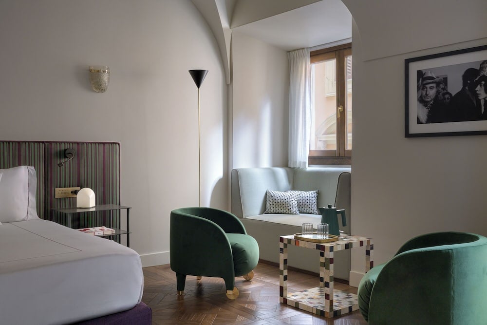 Emerald velvet armchairs and geometric side tables create intimate conversation nooks, while striped headboards and herringbone floors blend Sicilian charm with contemporary sophistication.