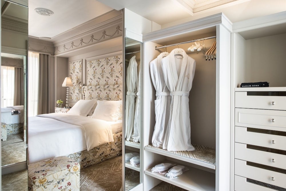 Crisp white robes await in custom wardrobes while floral wallpaper and coffered ceilings create an intimate sanctuary above the Spanish Steps.