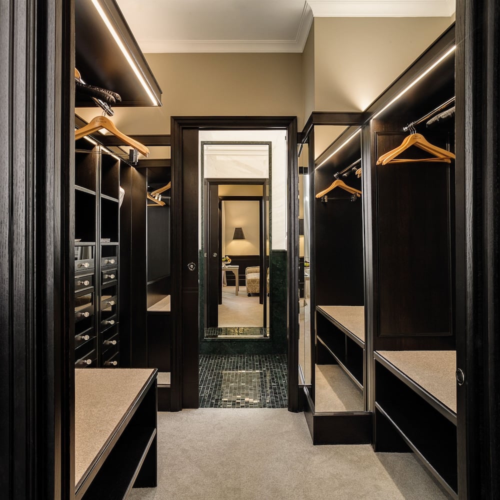 Dark wood cabinetry and LED strip lighting create an intimate walk-in closet where Italian craftsmanship meets modern luxury in every carefully considered detail.