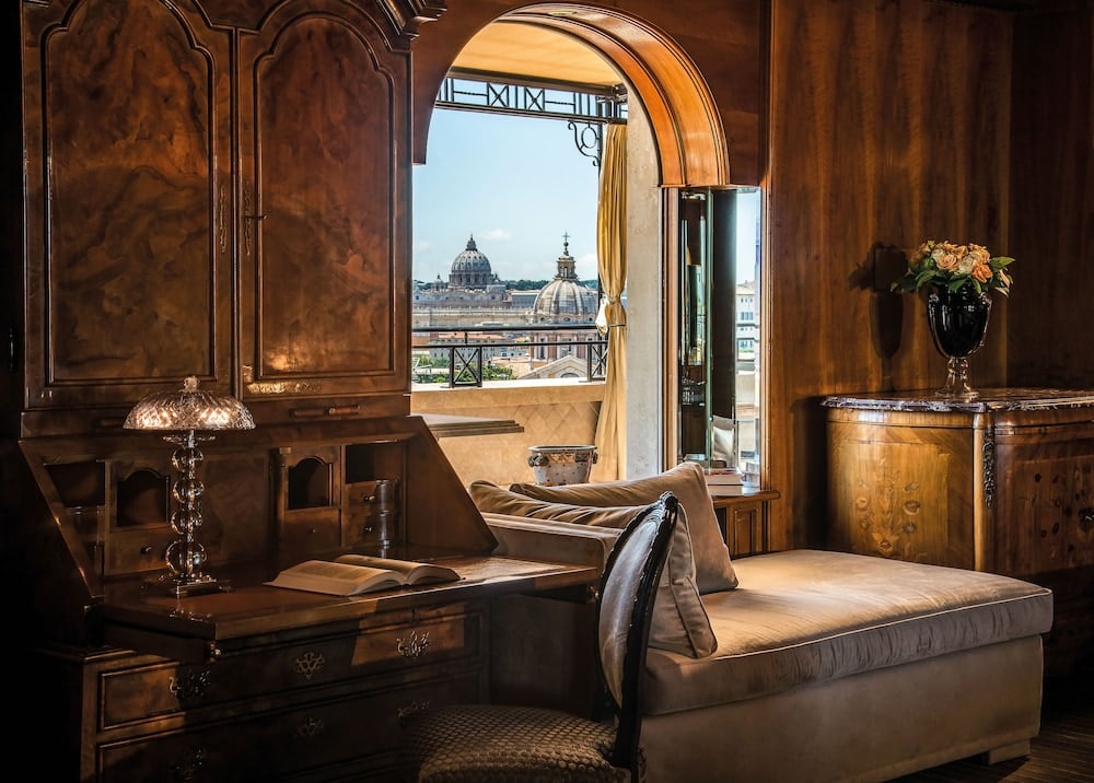 Walnut paneling and silk damask create an opulent sanctuary where Vatican domes frame the horizon through arched French doors, epitomizing Roman grandeur.