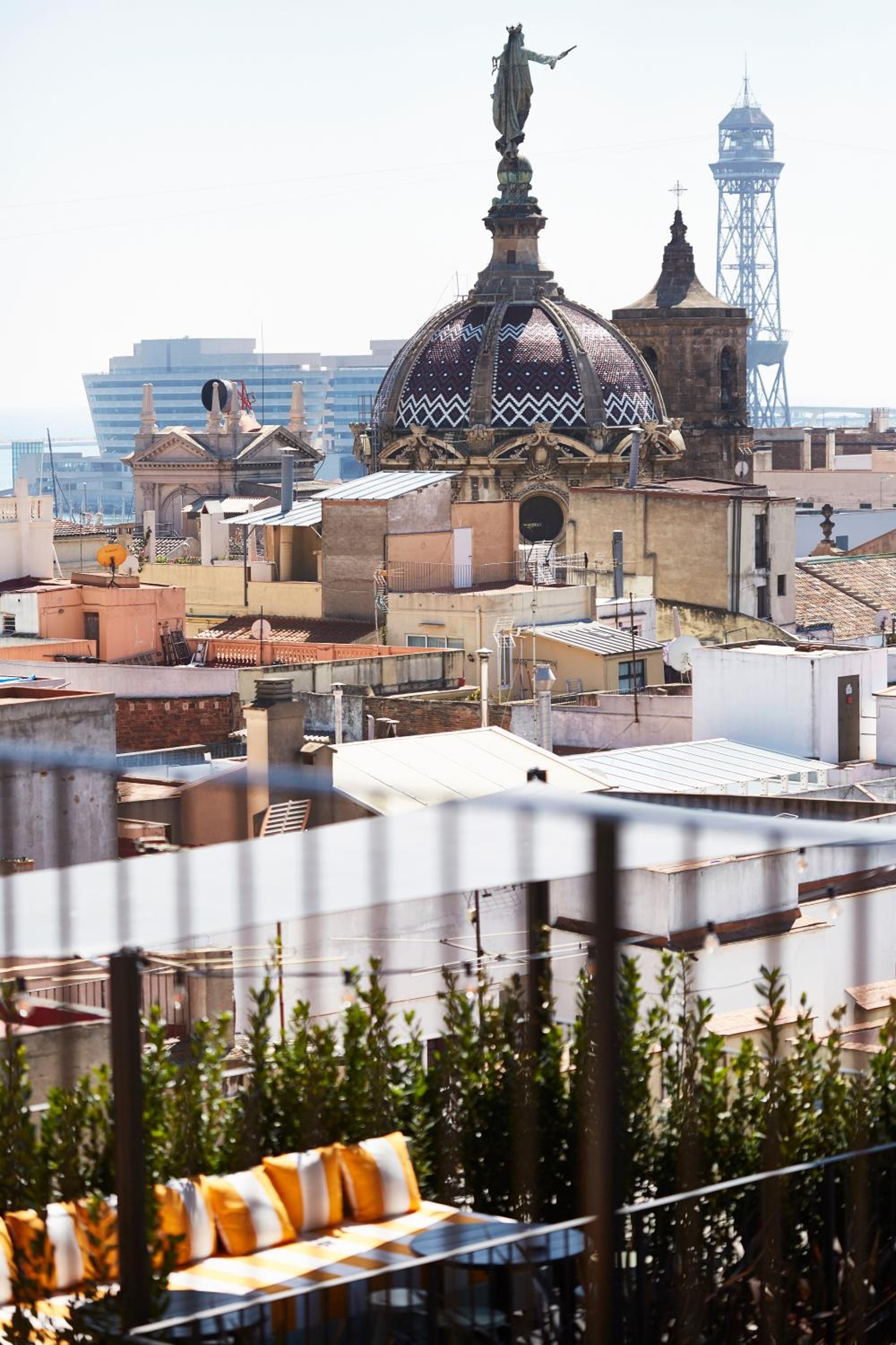 Orange cushions beckon from a private terrace overlooking Barcelona's tiled rooftops, where cathedral domes and azure Mediterranean light create an intimate urban sanctuary.