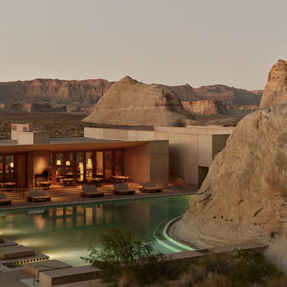 Desert architecture meets modern luxury as warm light spills from the resort's dramatic pavilions, while the infinity pool mirrors the ancient sandstone formations beyond.