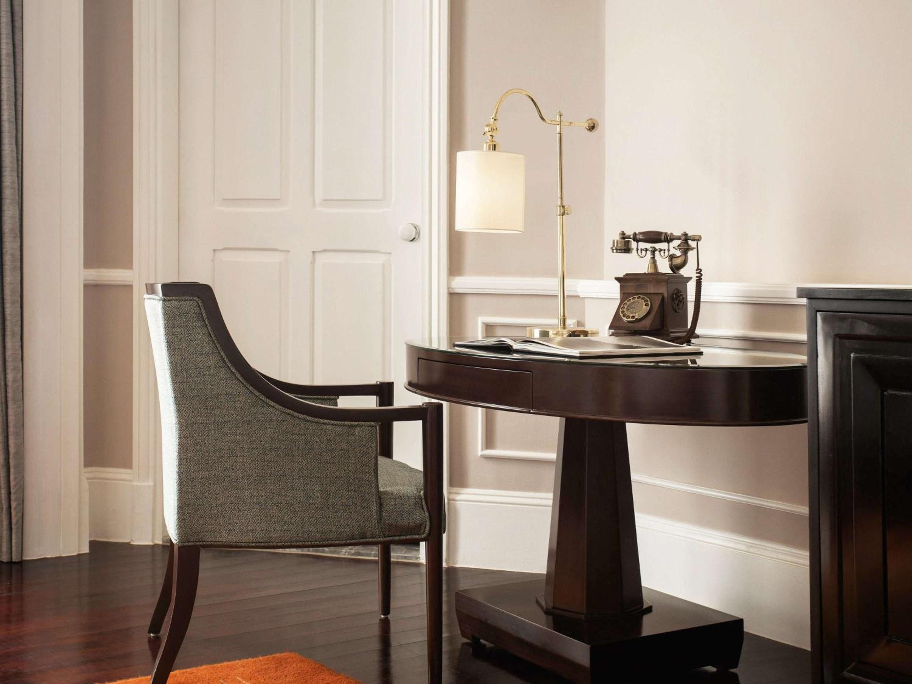 Warm brass lighting illuminates a mahogany writing desk where vintage rotary phones whisper of colonial elegance, while rich textures invite quiet contemplation.