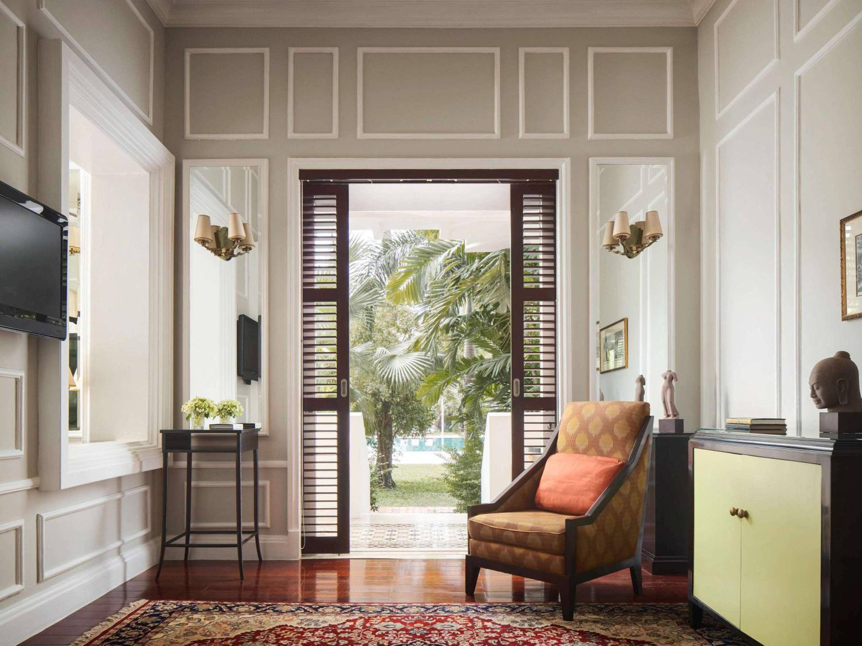 Colonial elegance meets tropical breeze in this sophisticated suite, where French doors frame swaying palms and rich hardwood floors reflect Cambodia's golden light.