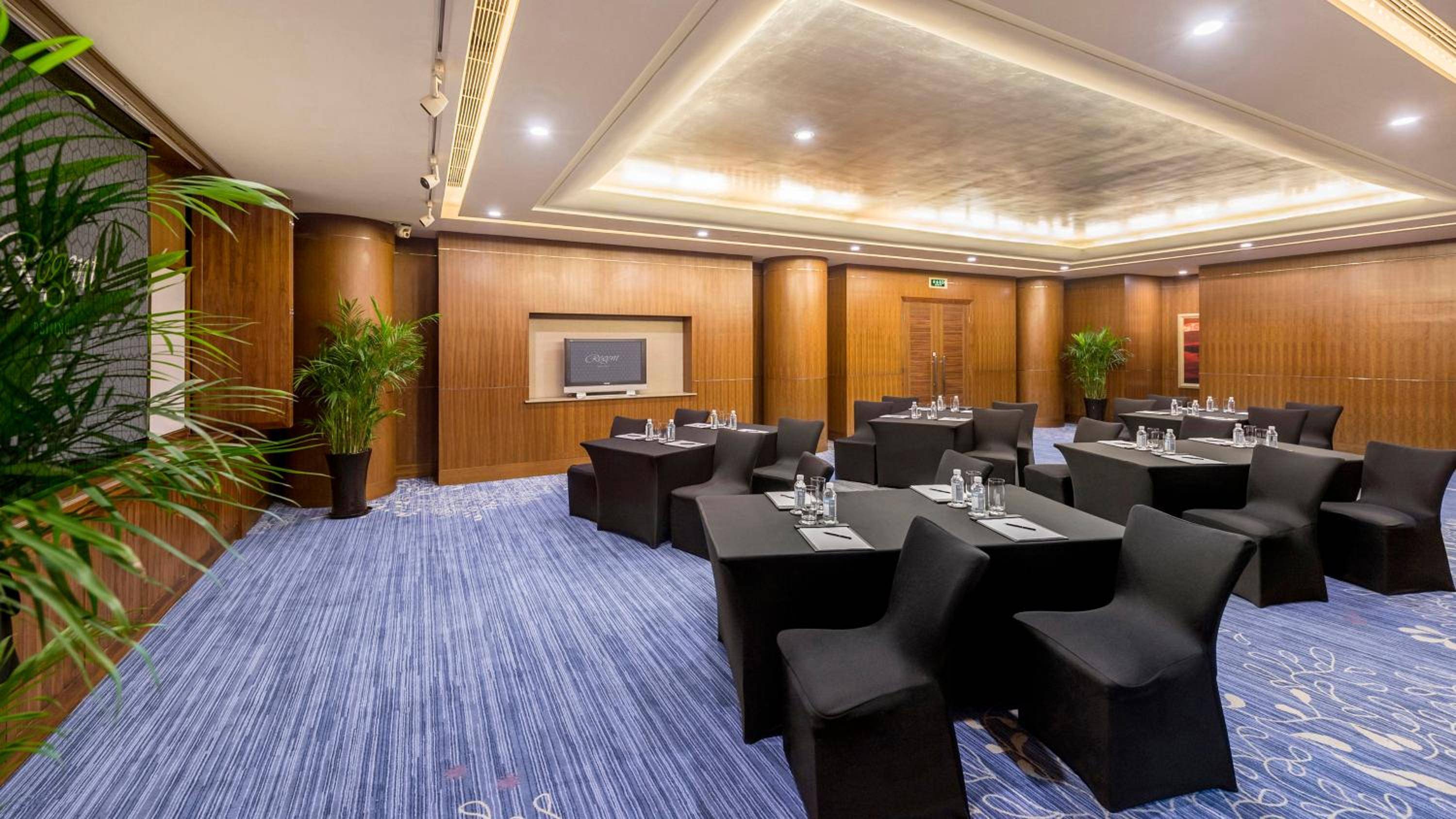 Warm wood paneling and contemporary furnishings create an intimate boardroom setting, where natural light filters through sophisticated ceiling details and tropical plants soften the corporate atmosphere.