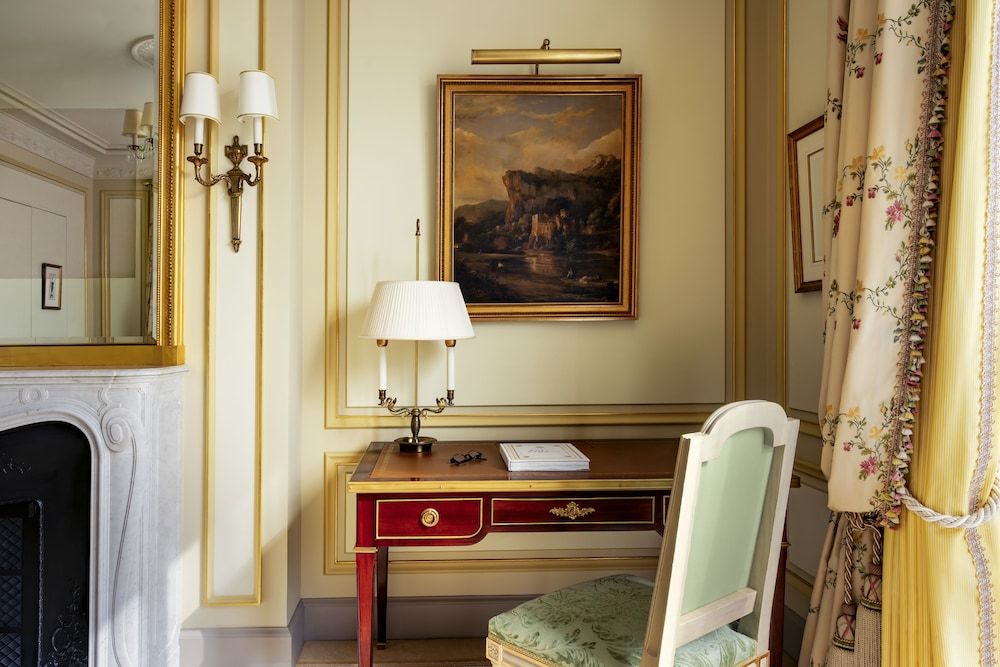 Gilded moldings frame an antique writing desk where silk-lined drawers and brass fittings whisper of handwritten correspondence beneath oil paintings and crystal sconces.