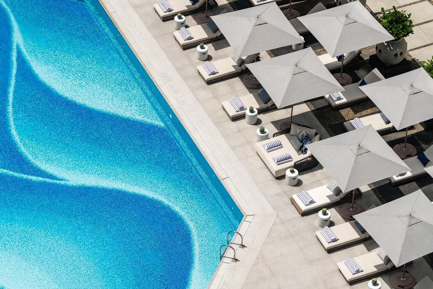 Pristine loungers and crisp white umbrellas line the infinity pool's edge, creating geometric shadows against sun-warmed stone in this serene poolside sanctuary.