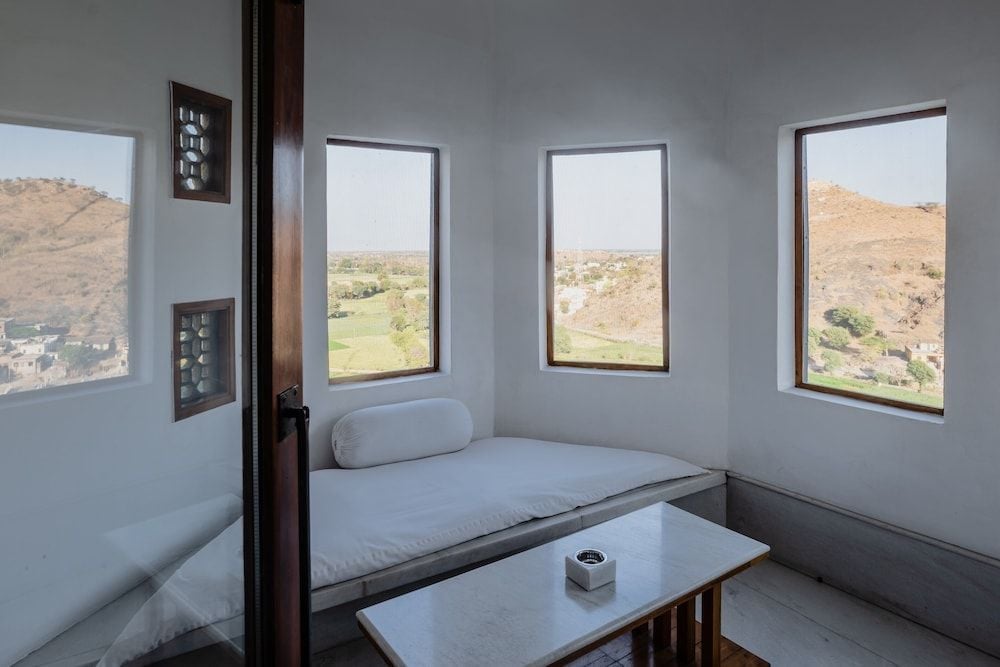 Built-in daybeds frame panoramic Aravalli Hills vistas through minimalist windows, where morning light illuminates this serene corner retreat's clean lines and neutral palette.