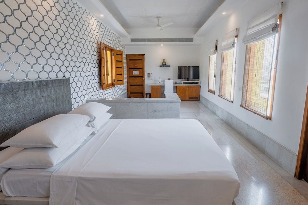 Crisp white linens contrast beautifully with geometric wallpaper and polished terrazzo floors in this airy suite, where traditional jali screens filter golden Rajasthani light.