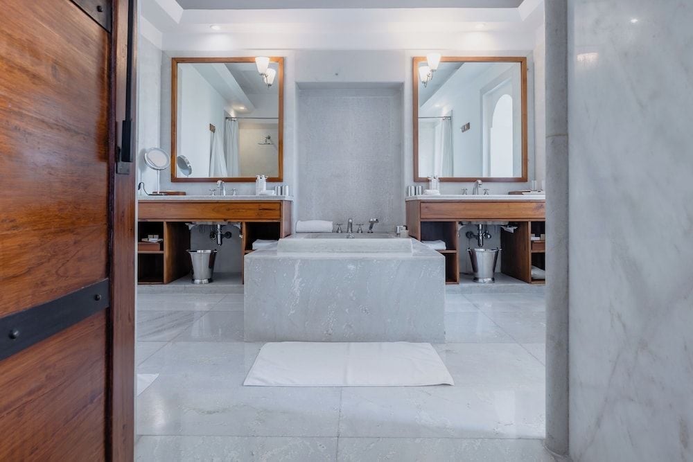 Marble surfaces and warm wood vanities create a serene sanctuary, where twin basins frame a sculptural soaking tub beneath soft recessed lighting.