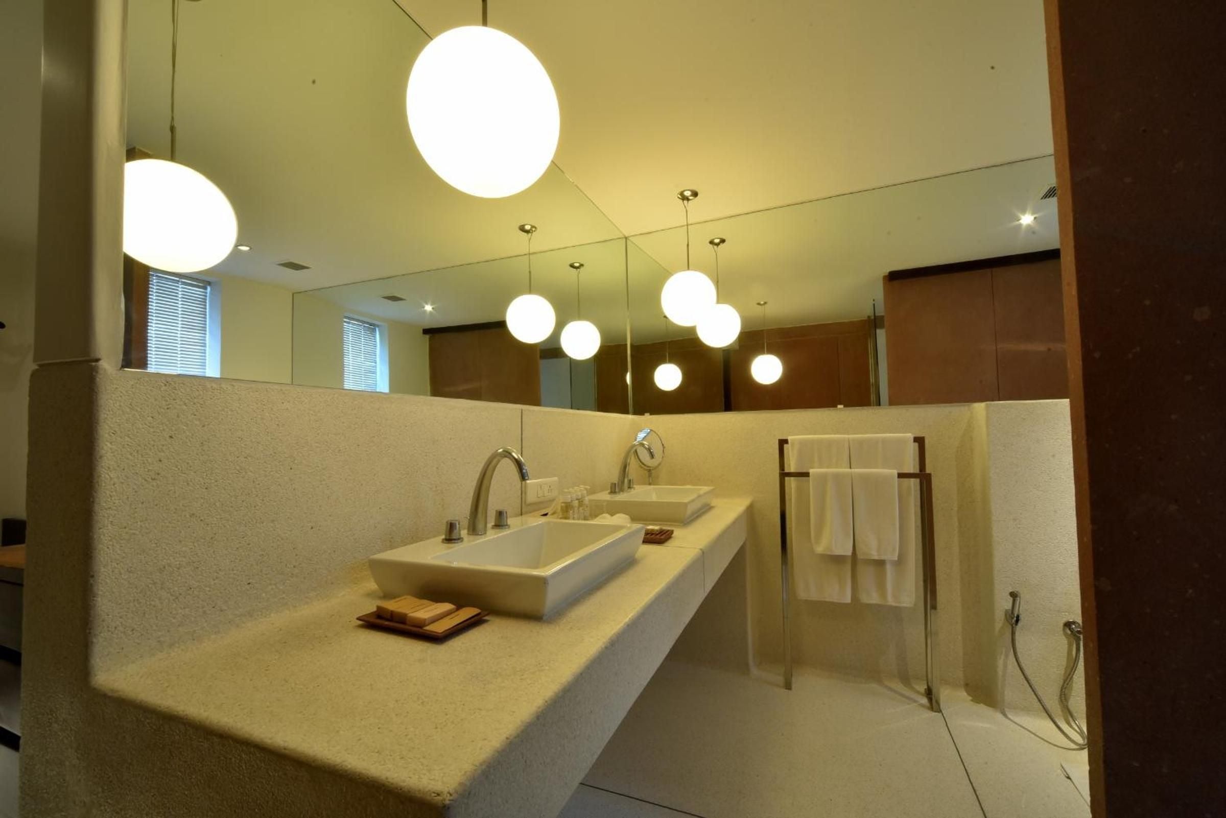 Spherical pendant lights dance above minimalist basin sinks, while warm stone surfaces and sleek fixtures create a spa-like sanctuary of contemporary luxury.