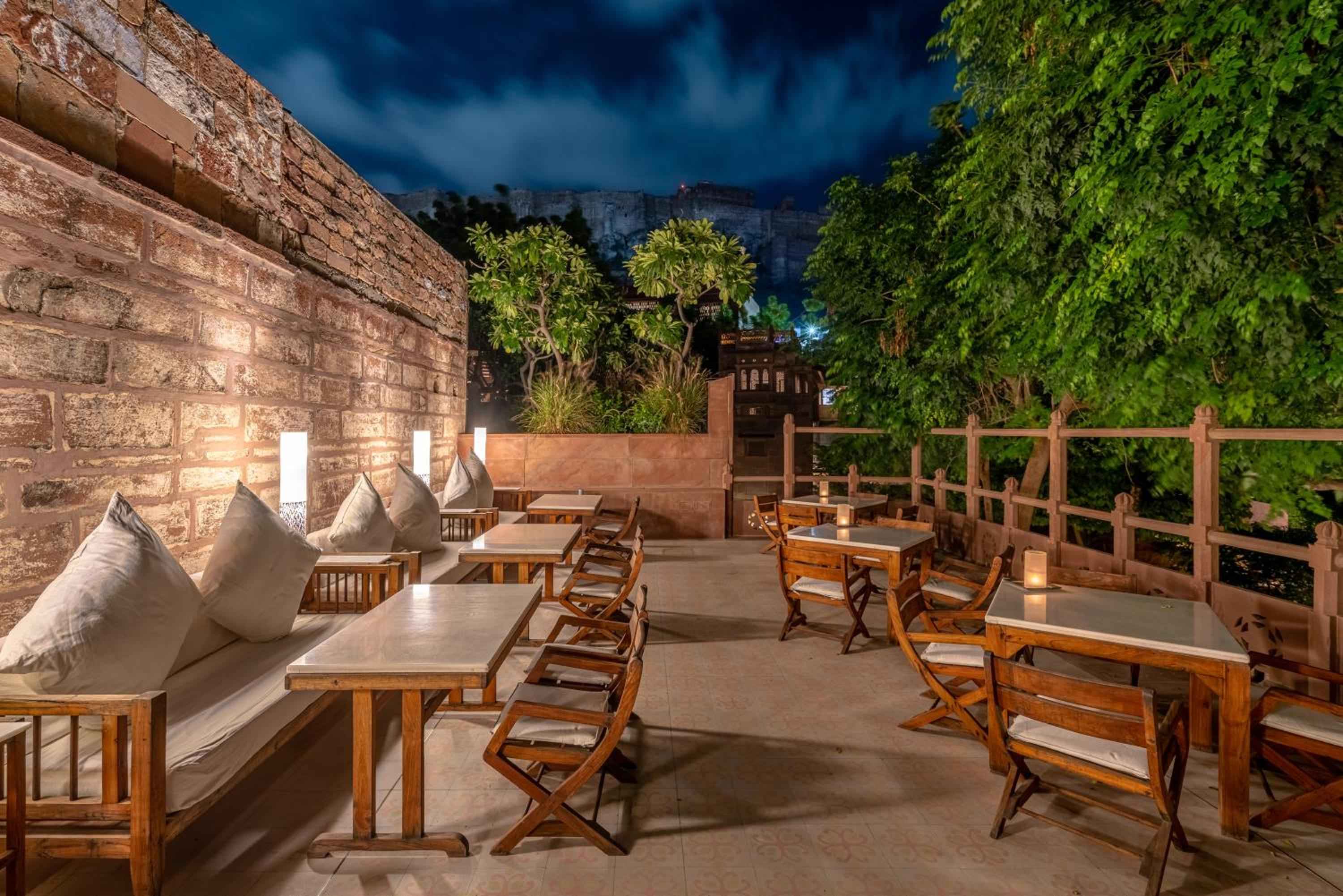 Candlelit tables and plush cushions create an intimate rooftop dining experience, with ancient sandstone walls and Mehrangarh Fort's imposing silhouette completing this magical Jodhpur evening.