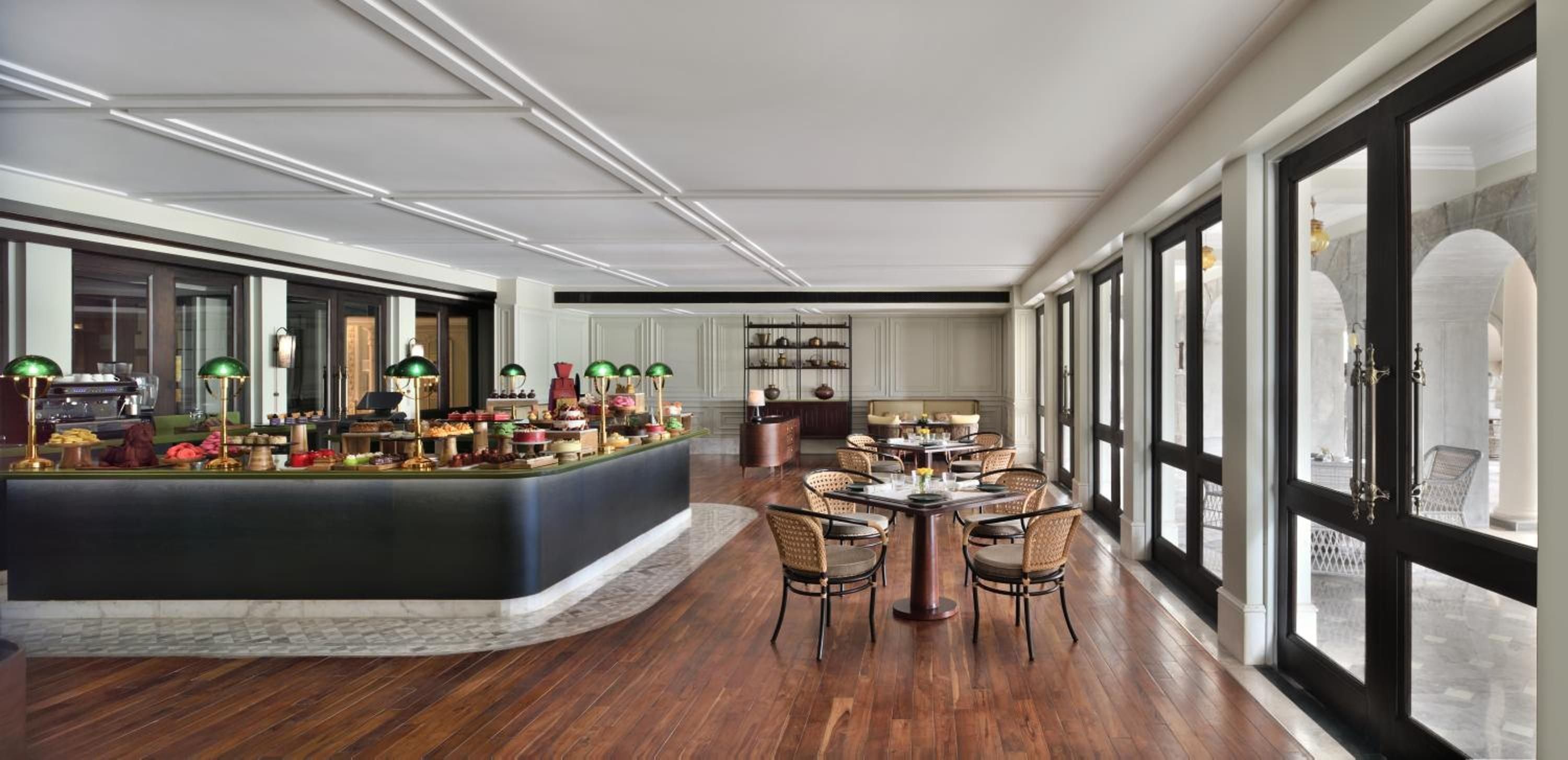 Emerald banker's lamps cast intimate pools of light over the breakfast buffet, while dark wood floors and flowing curtains create an elegant morning ritual overlooking manicured gardens.