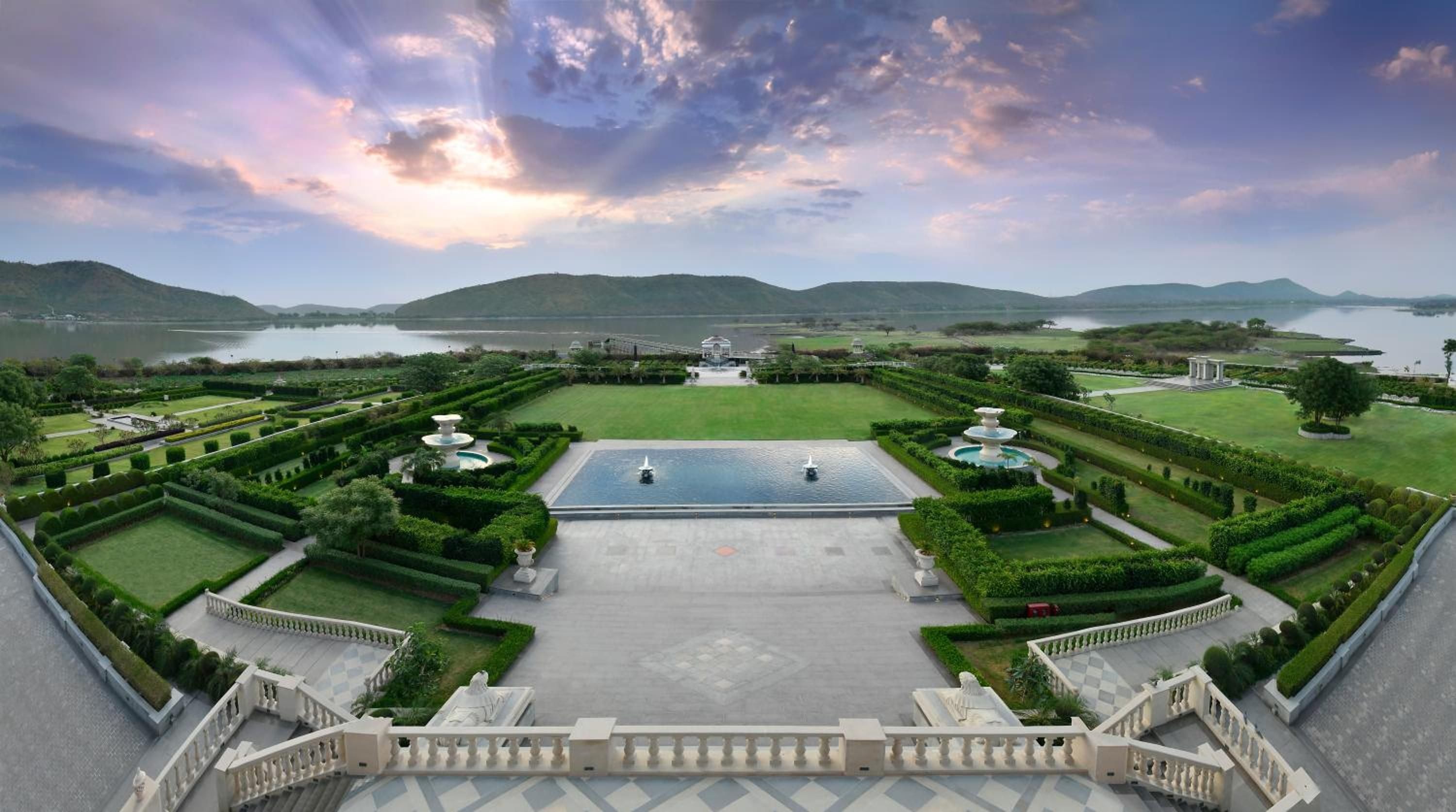 Manicured parterre gardens stretch toward distant hills, their geometric precision softened by twilight's purple glow above this palatial lakeside retreat.