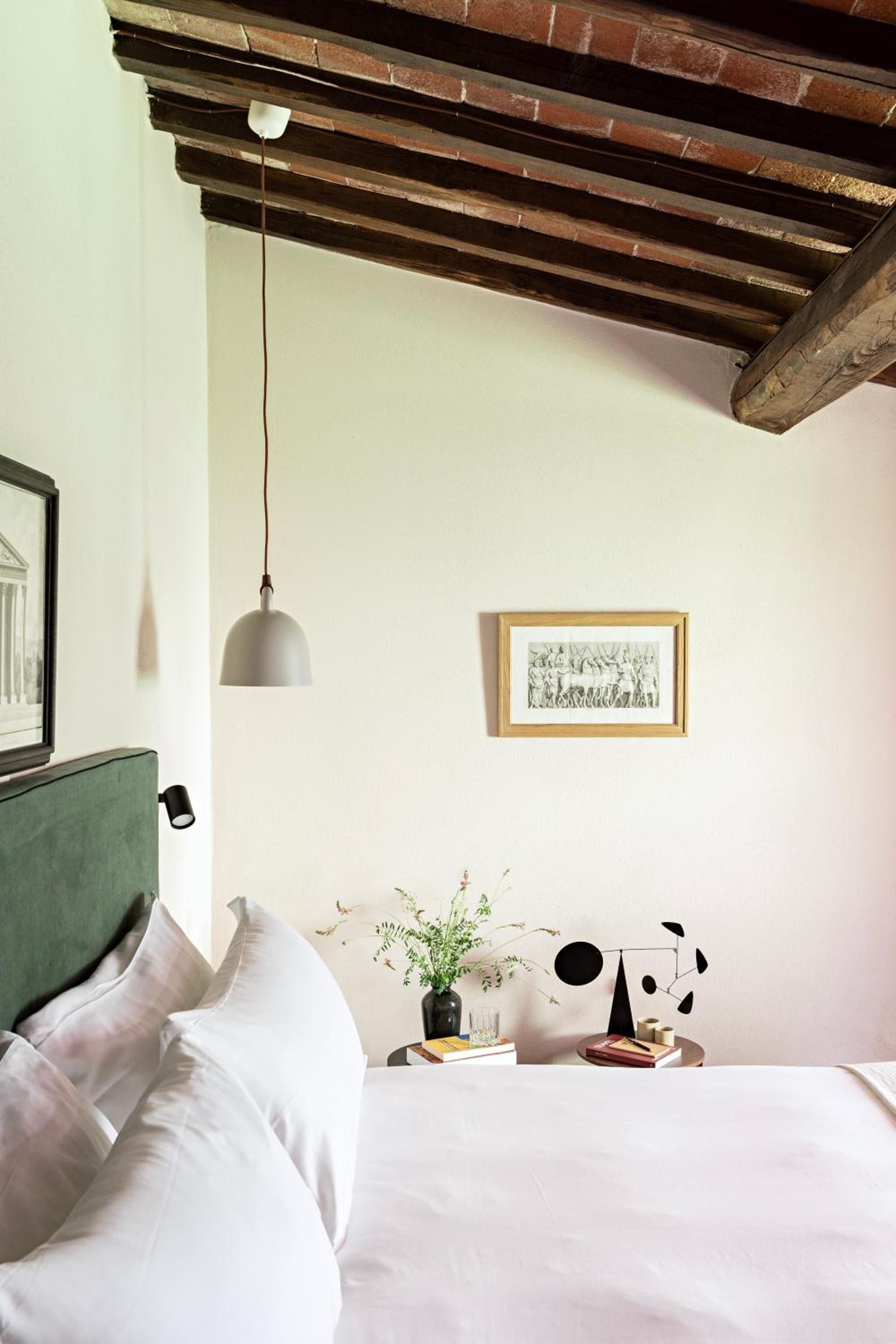 Exposed terracotta ceiling beams frame this intimate bedroom sanctuary, where sage-green headboards meet crisp linens and thoughtfully curated bedside vignettes create rustic-modern harmony.