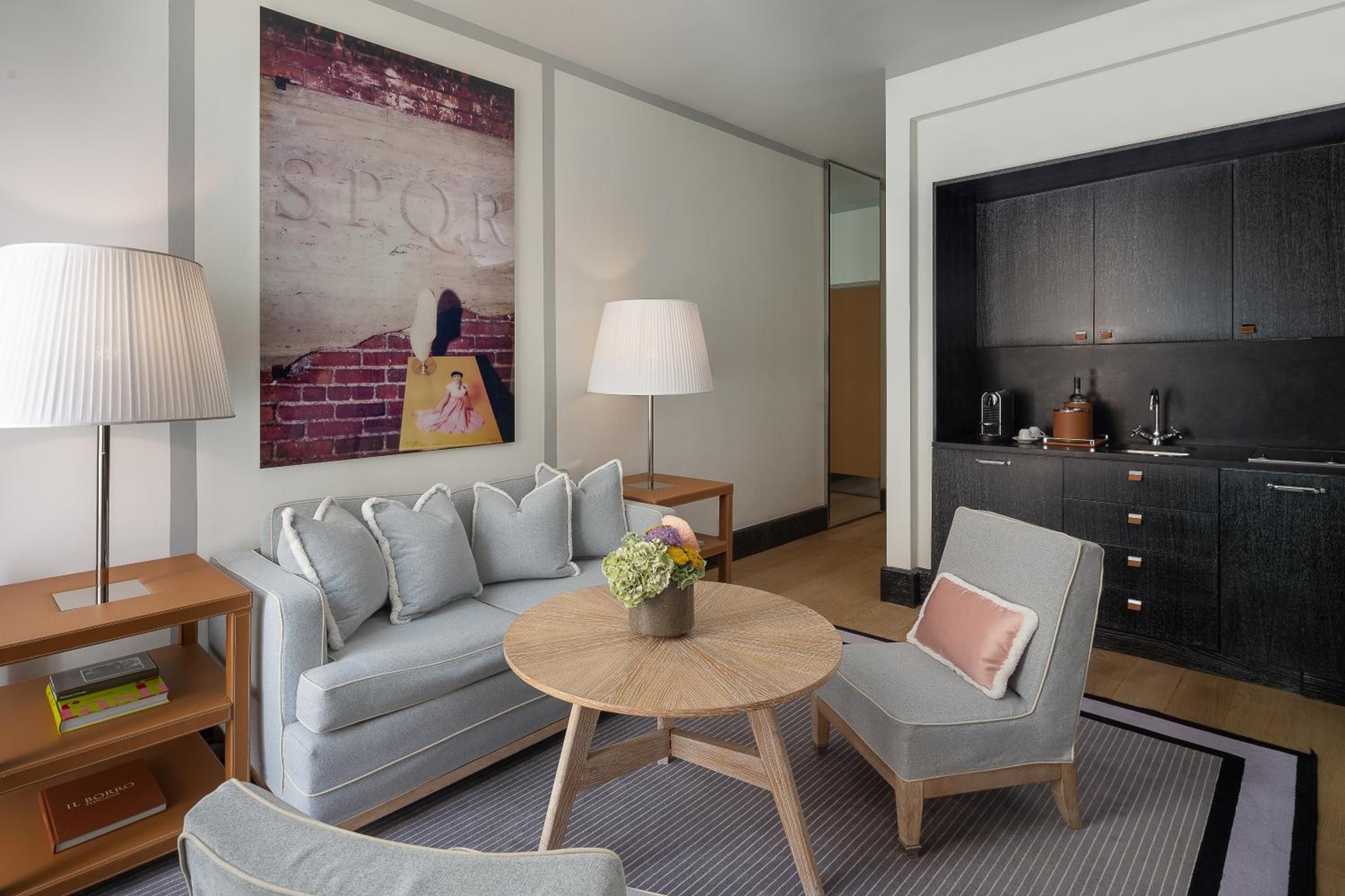 Contemporary Roman elegance unfolds in this sophisticated suite, where warm wood tones meet cool grey textiles beneath striking artwork celebrating the Eternal City's layered history.