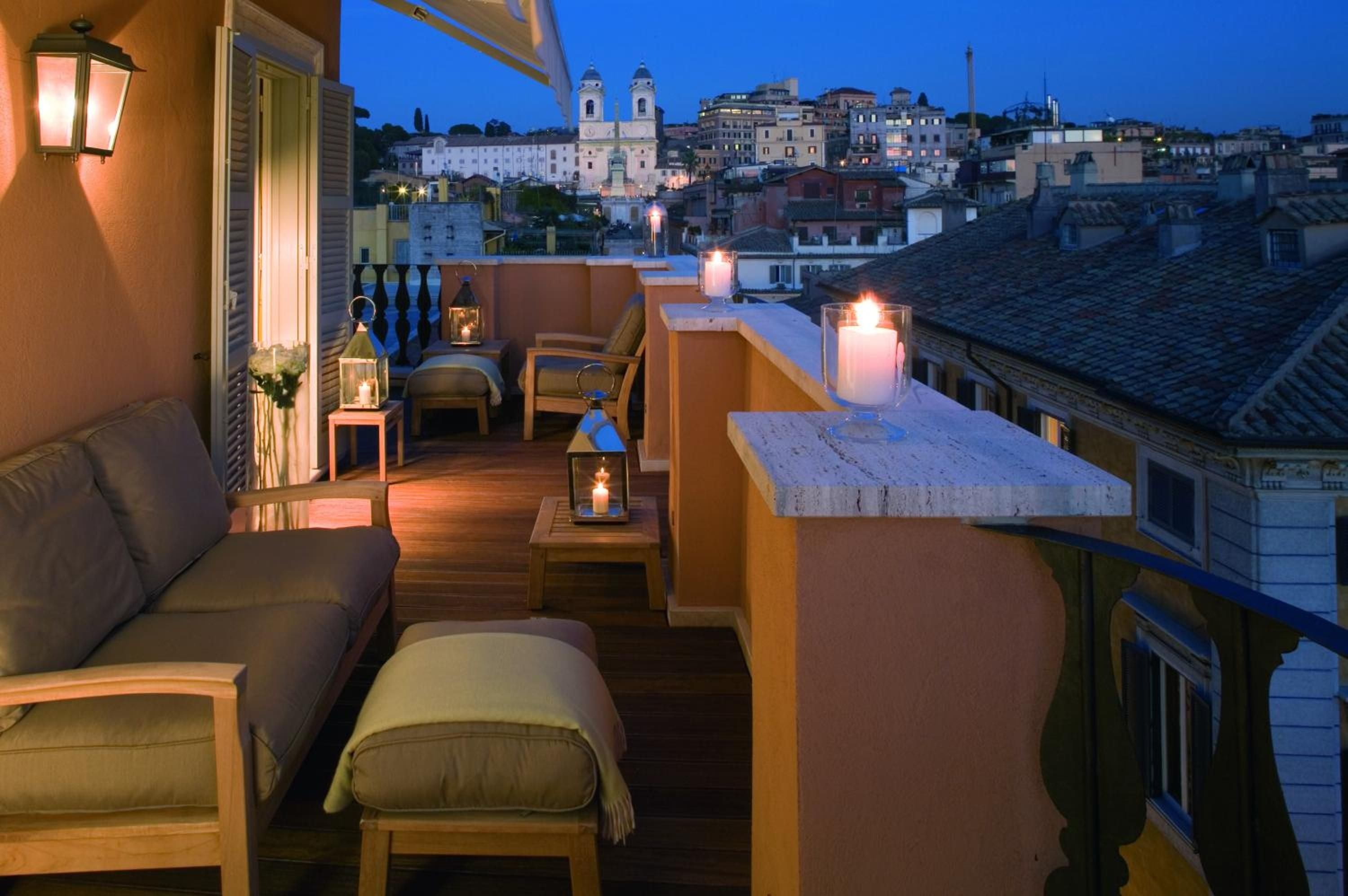 Candlelit lanterns flicker across the intimate rooftop terrace as Rome's ancient skyline glows in twilight, creating an enchanting backdrop for evening aperitivos.