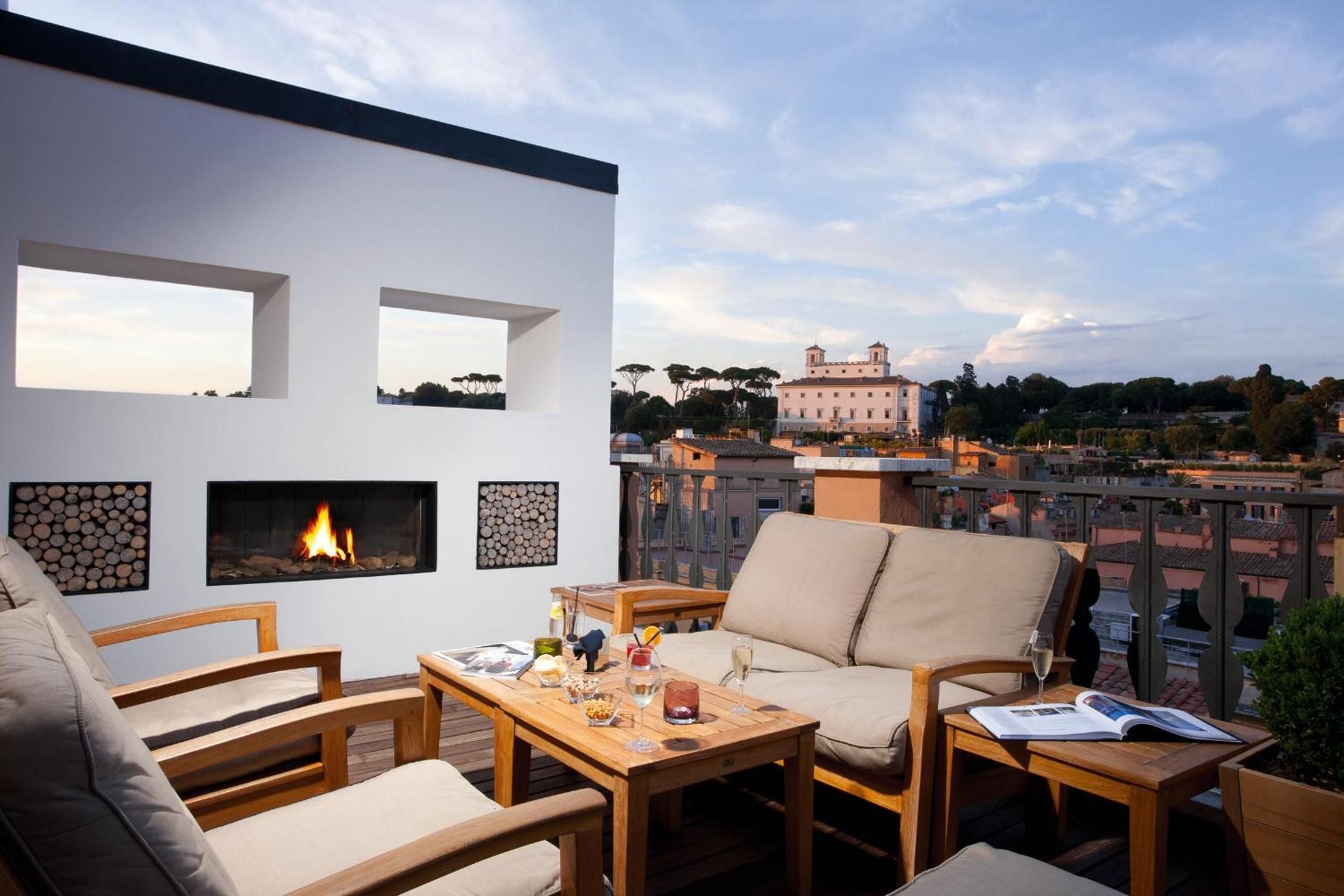 Crackling flames warm the rooftop terrace as Rome's terracotta rooftops stretch toward Villa Medici, creating an intimate urban sanctuary above the Eternal City.