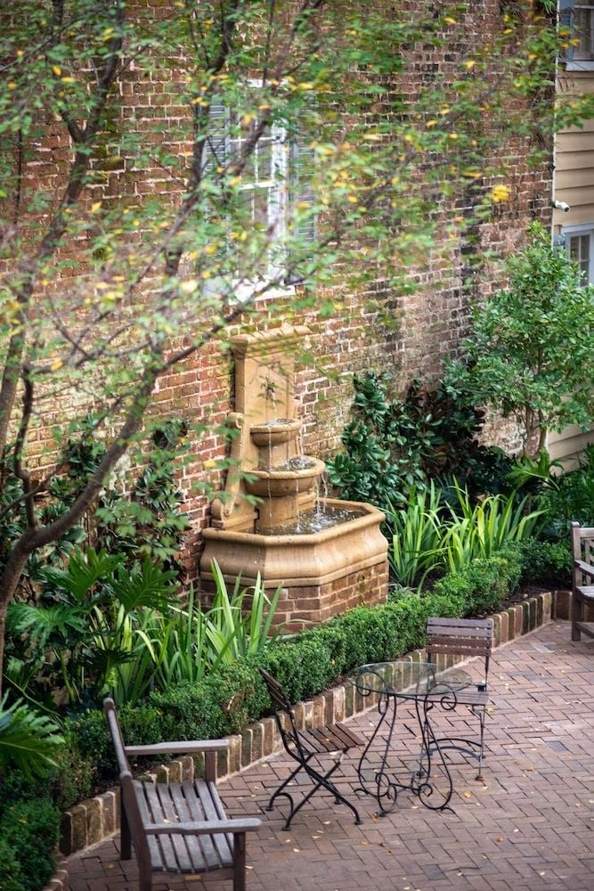 Sunlight filters through leafy branches onto the hotel's intimate brick courtyard, where a tiered fountain whispers softly beside wrought-iron café chairs on weathered pavers.