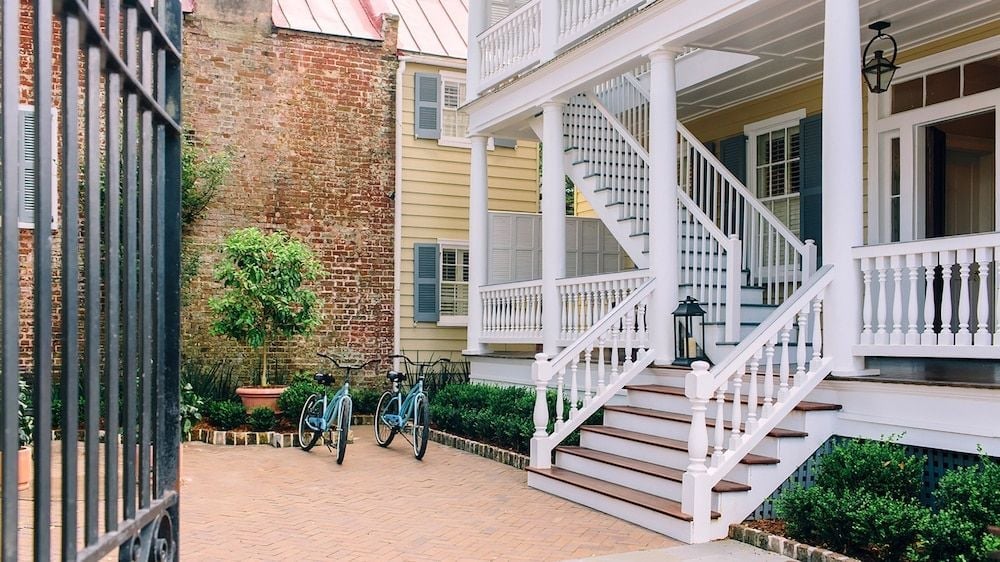 Mint-green bicycles rest against weathered brick walls while white verandas cascade down historic Charleston townhouses, creating an intimate courtyard sanctuary.