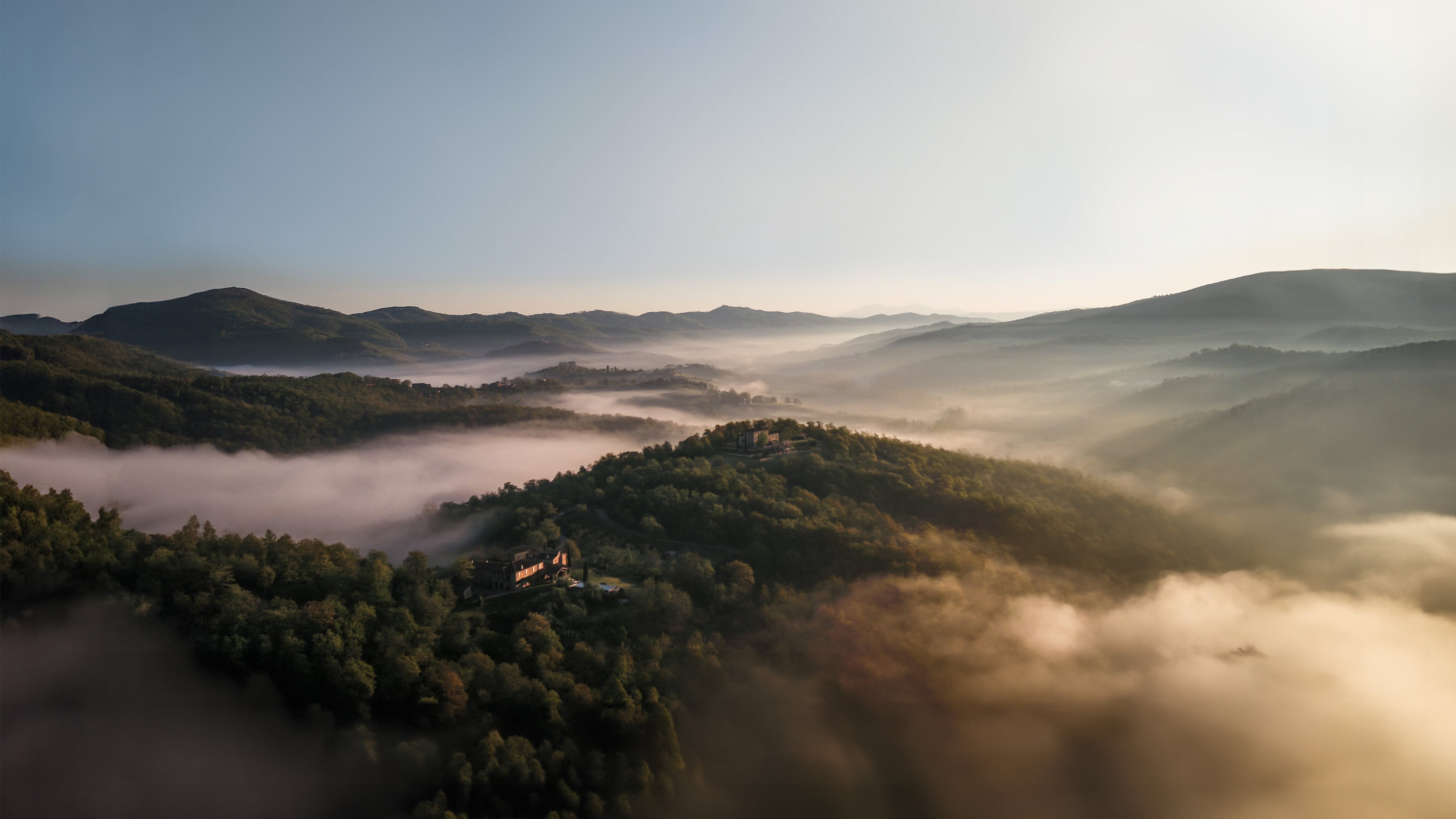 Morning mist drifts through Umbrian valleys as hilltop structures emerge like ancient sentinels from the fog, their terracotta roofs catching golden dawn light.