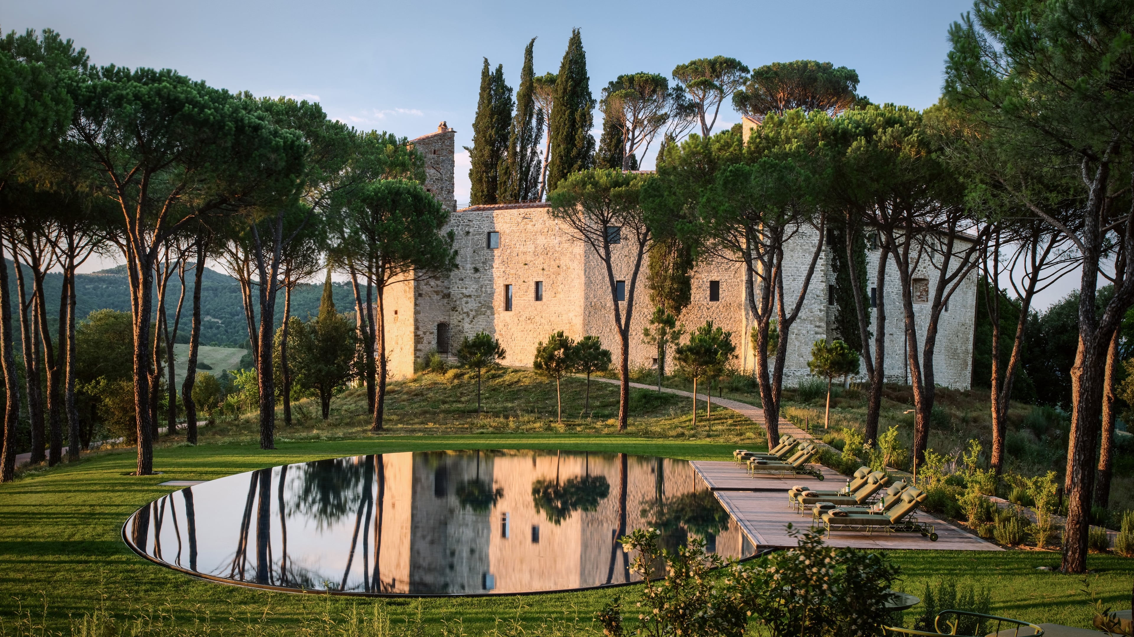 Golden hour light bathes the medieval castello while its reflection shimmers in the infinity pool, creating a perfect mirror of Umbrian stone and cypress trees.