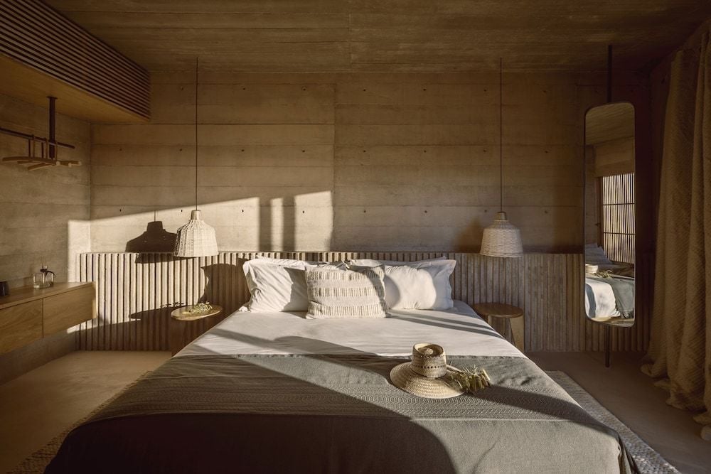Sunlight streams through bamboo screens onto raw concrete walls and crisp linens, creating an intimate cocoon where desert minimalism meets thoughtful luxury in each carefully curated suite.