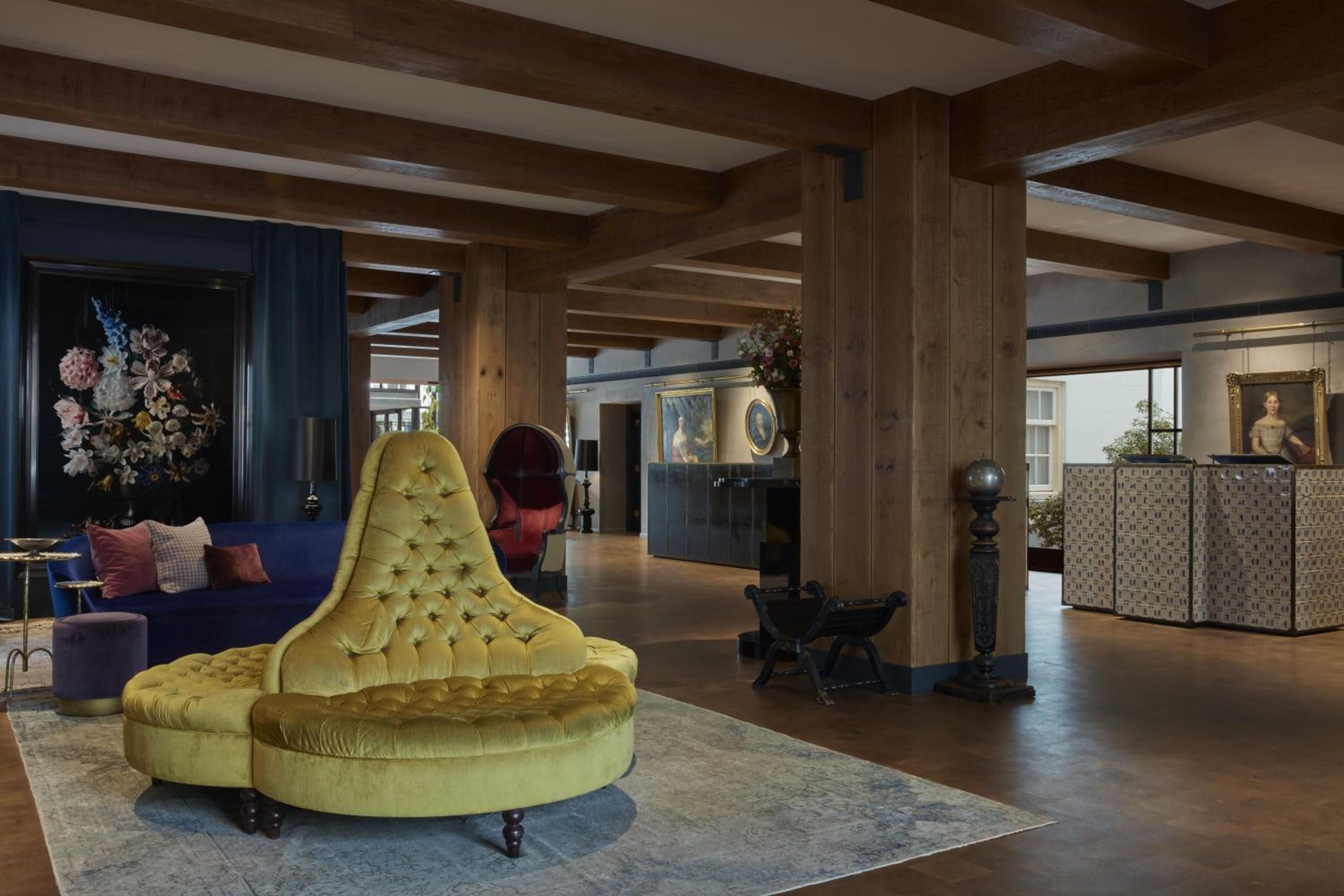 Exposed timber beams frame jewel-toned seating and Dutch masterworks in this canal house lobby, where chartreuse velvet meets centuries-old craftsmanship.